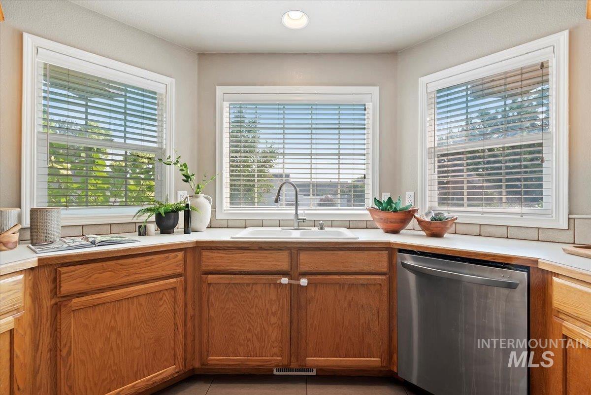 Kitchen with light countertops, stainless steel dishwasher, brown cabinets, and tile patterned flooring