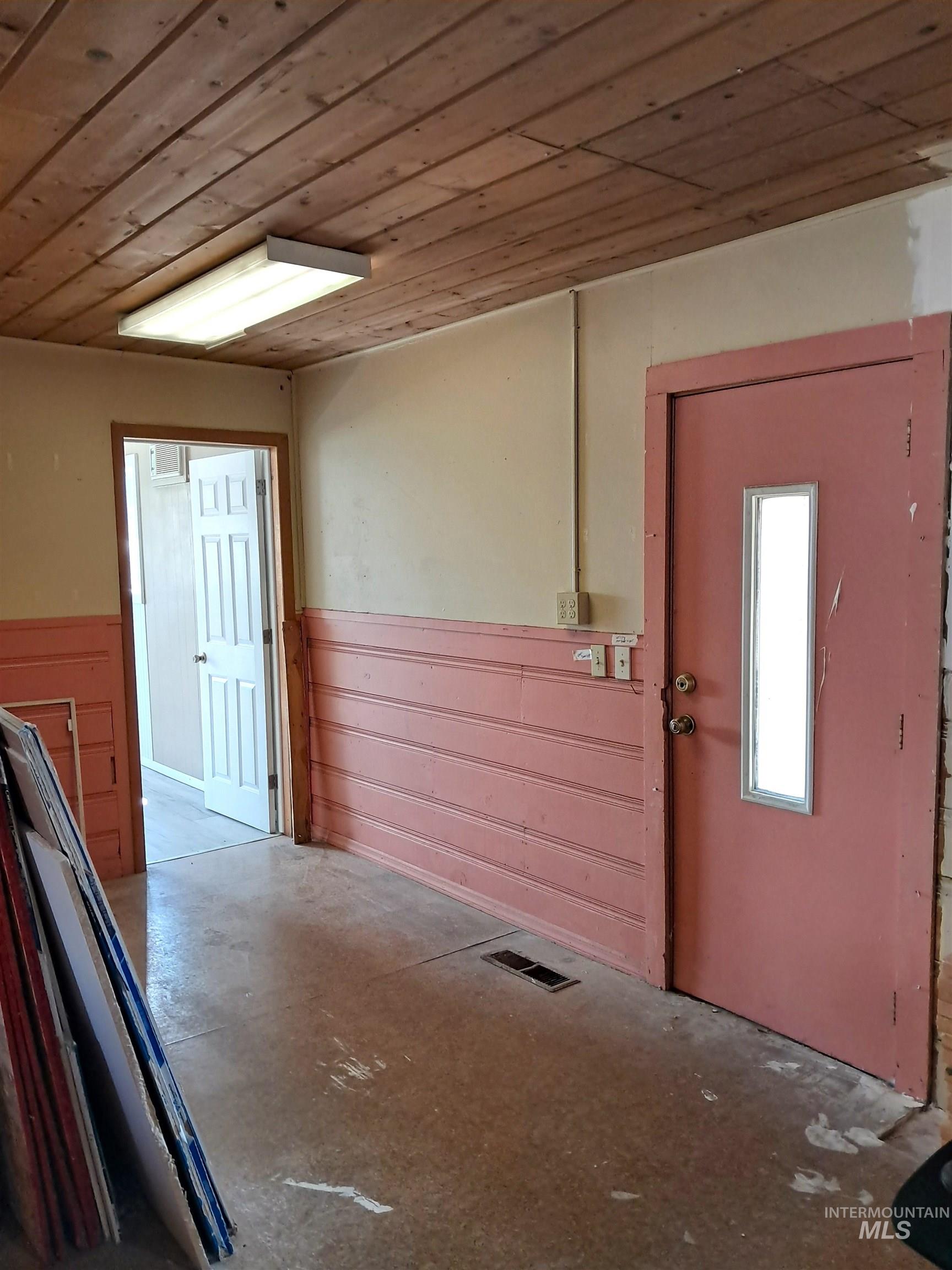 Doorway to outside featuring wooden ceiling, concrete floors, and a wainscoted wall
