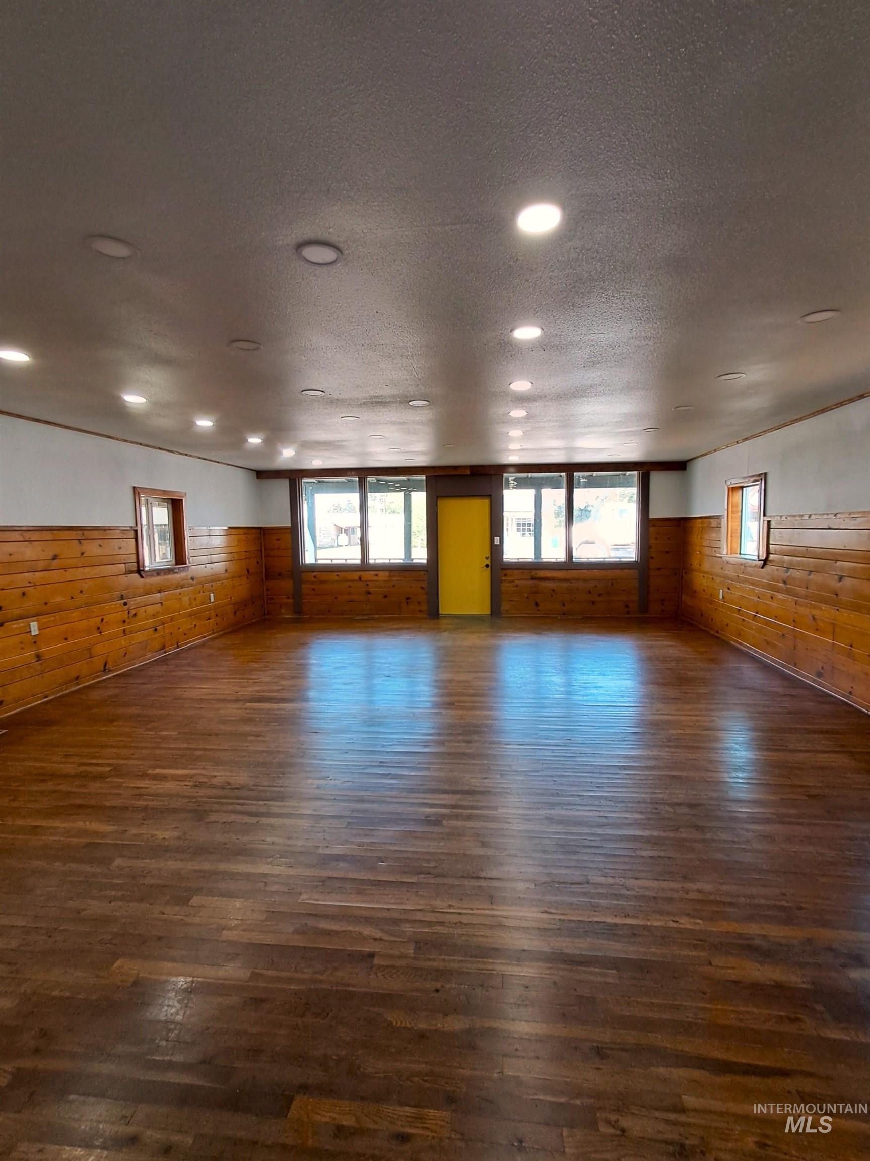 Unfurnished room featuring dark wood-type flooring, wooden walls, and a textured ceiling