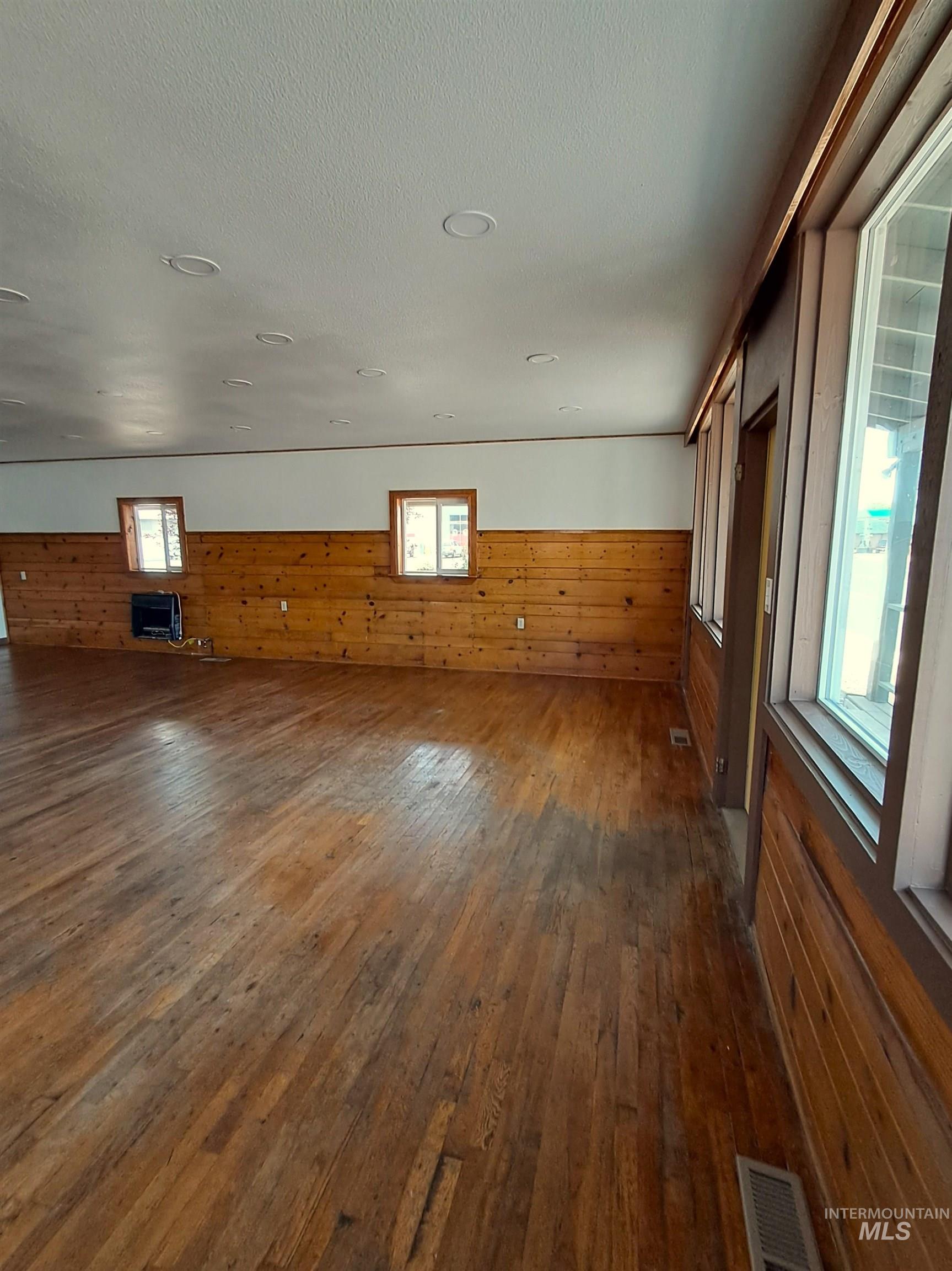 Unfurnished living room featuring dark wood-style floors, healthy amount of natural light, wooden walls, and a textured ceiling