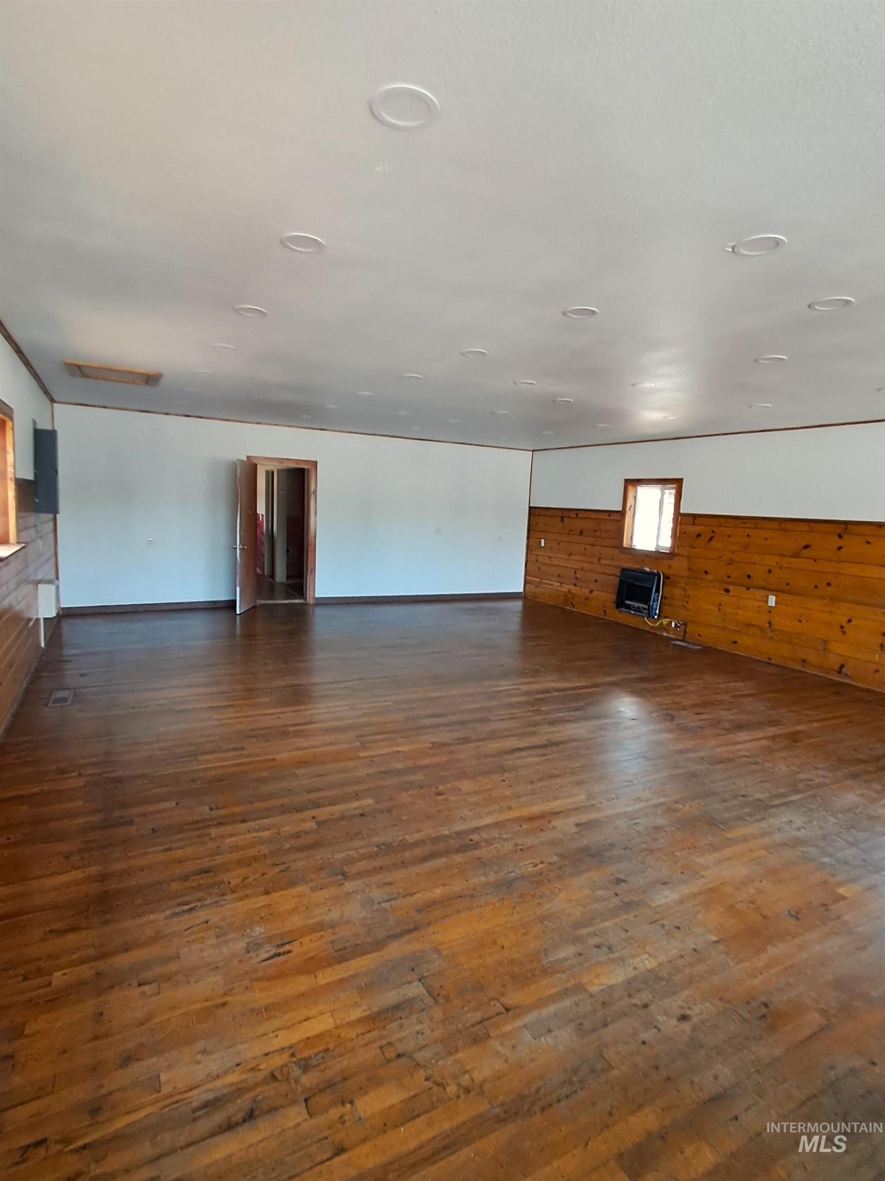Unfurnished living room featuring wooden walls, dark wood finished floors, and heating unit