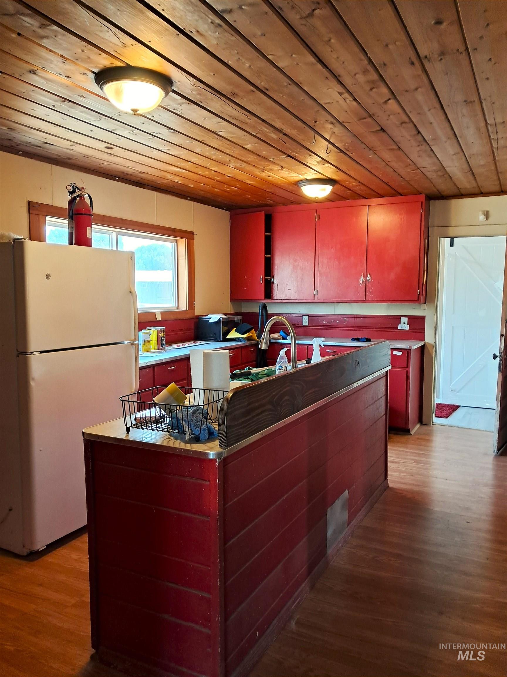 Kitchen with wooden ceiling, freestanding refrigerator, open shelves, dark wood-type flooring, and red cabinetry