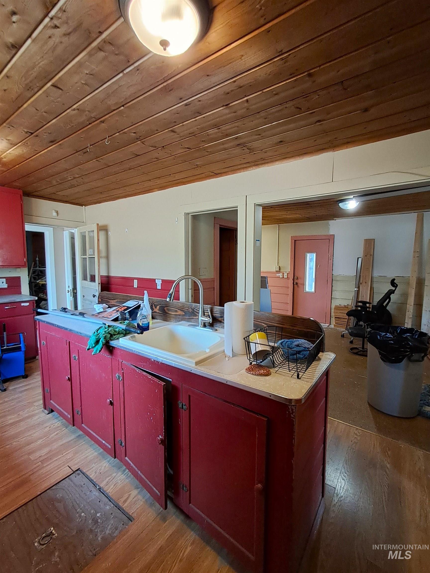 Kitchen with red cabinets, wood ceiling, light countertops, light wood-style floors, and reddish brown cabinets