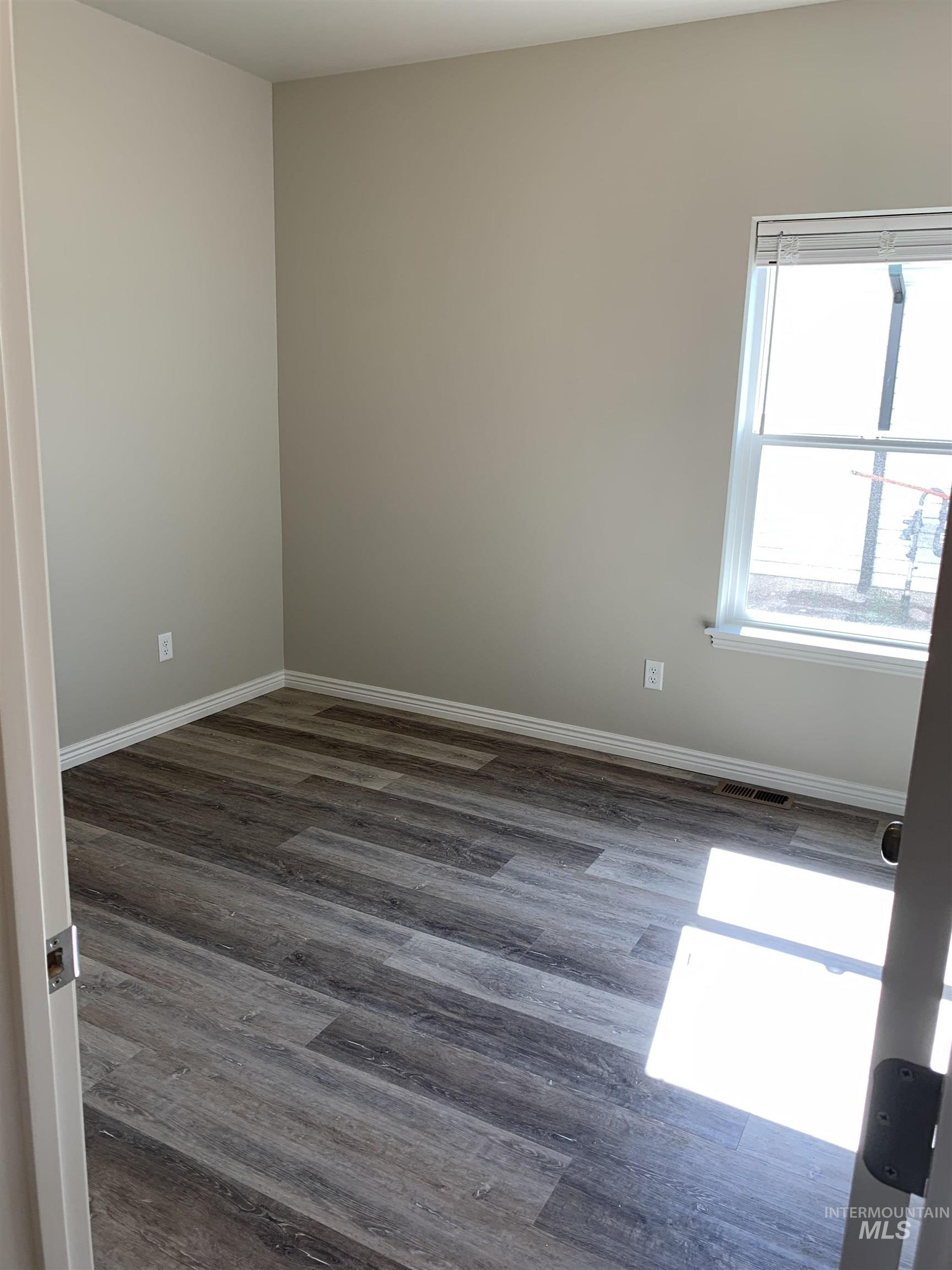 Empty room featuring dark wood-style floors and baseboards