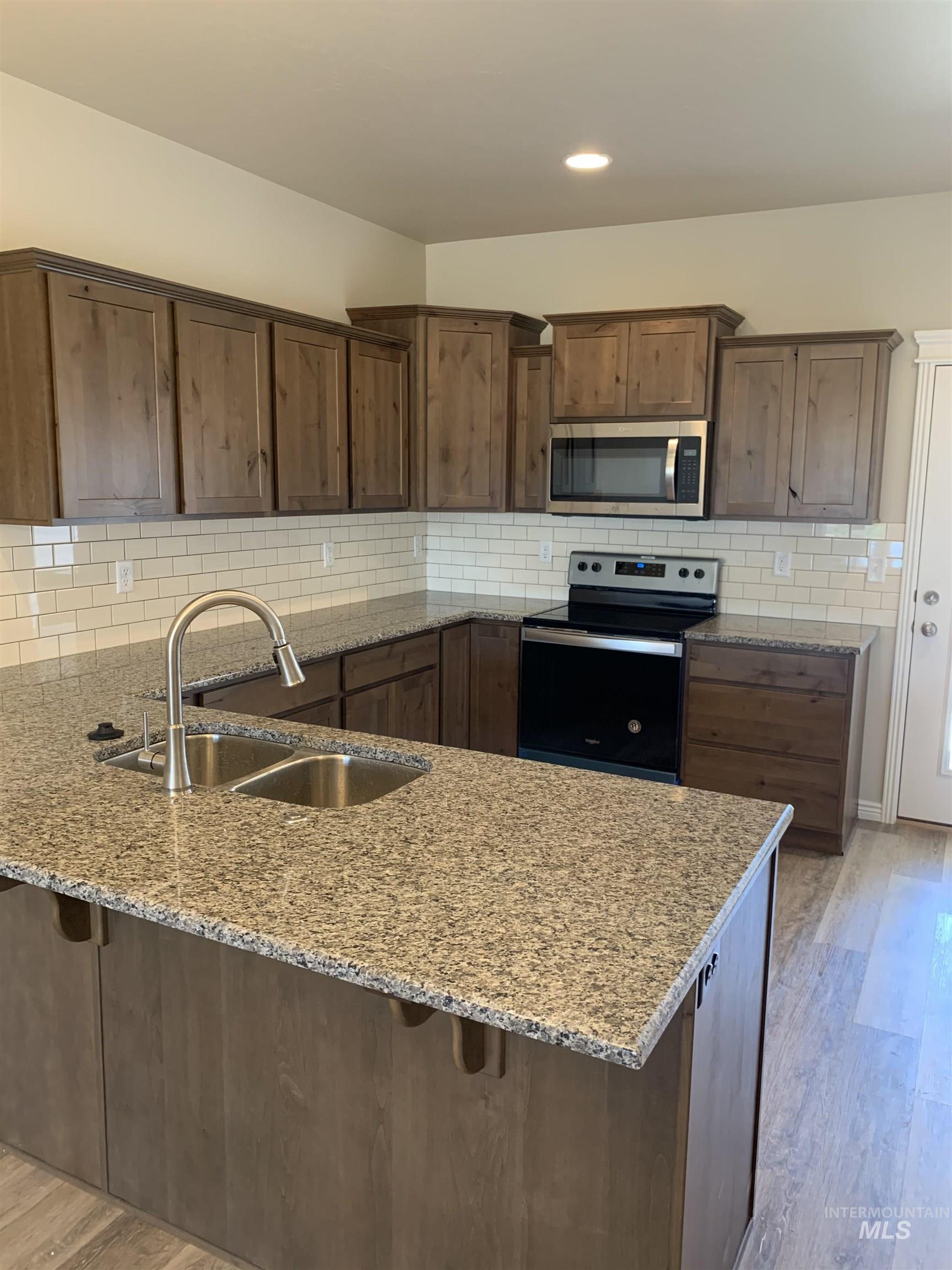Kitchen featuring light wood finished floors, a peninsula, stainless steel appliances, light stone counters, and recessed lighting