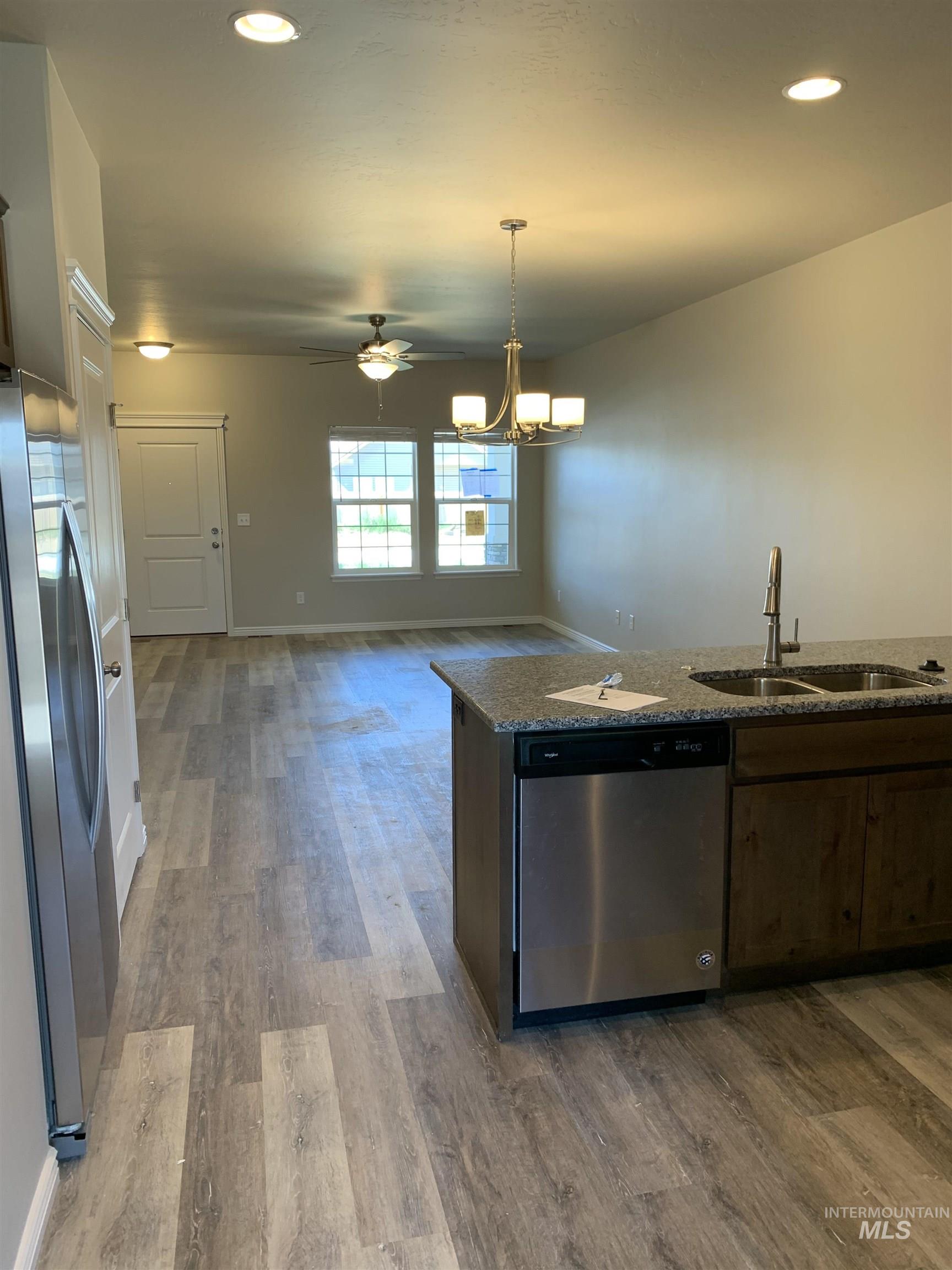Kitchen featuring stainless steel appliances, ceiling fan, light wood-style flooring, pendant lighting, and dark stone countertops