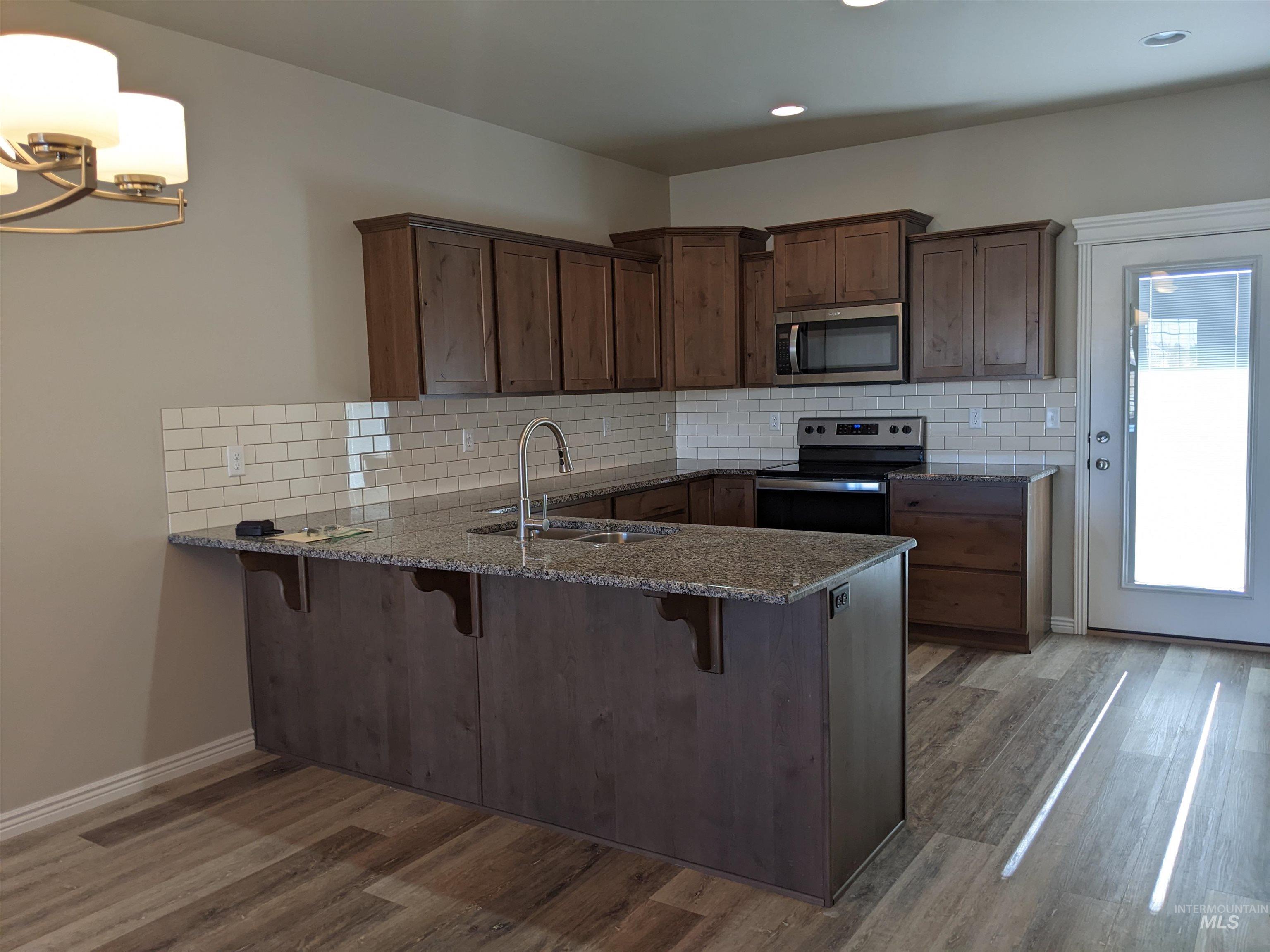 Kitchen featuring dark stone countertops, a kitchen bar, backsplash, stainless steel appliances, and a peninsula