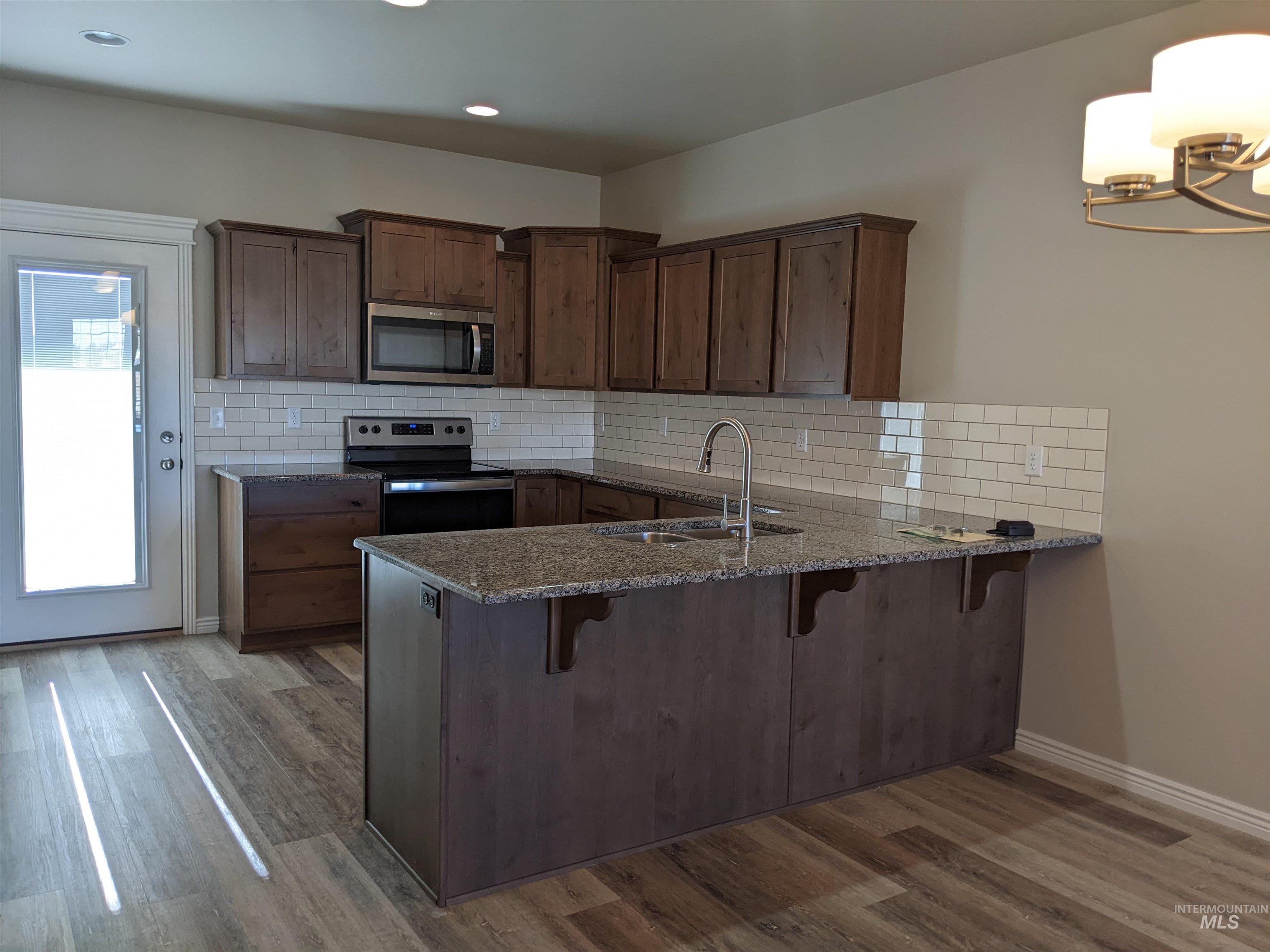 Kitchen with a kitchen bar, dark stone counters, appliances with stainless steel finishes, backsplash, and a peninsula