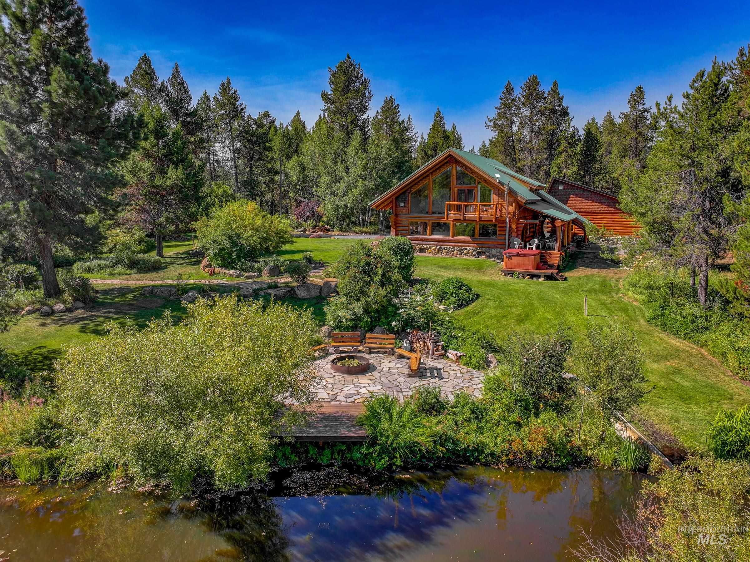Back of property featuring a water view, a fire pit, a patio, and a lawn