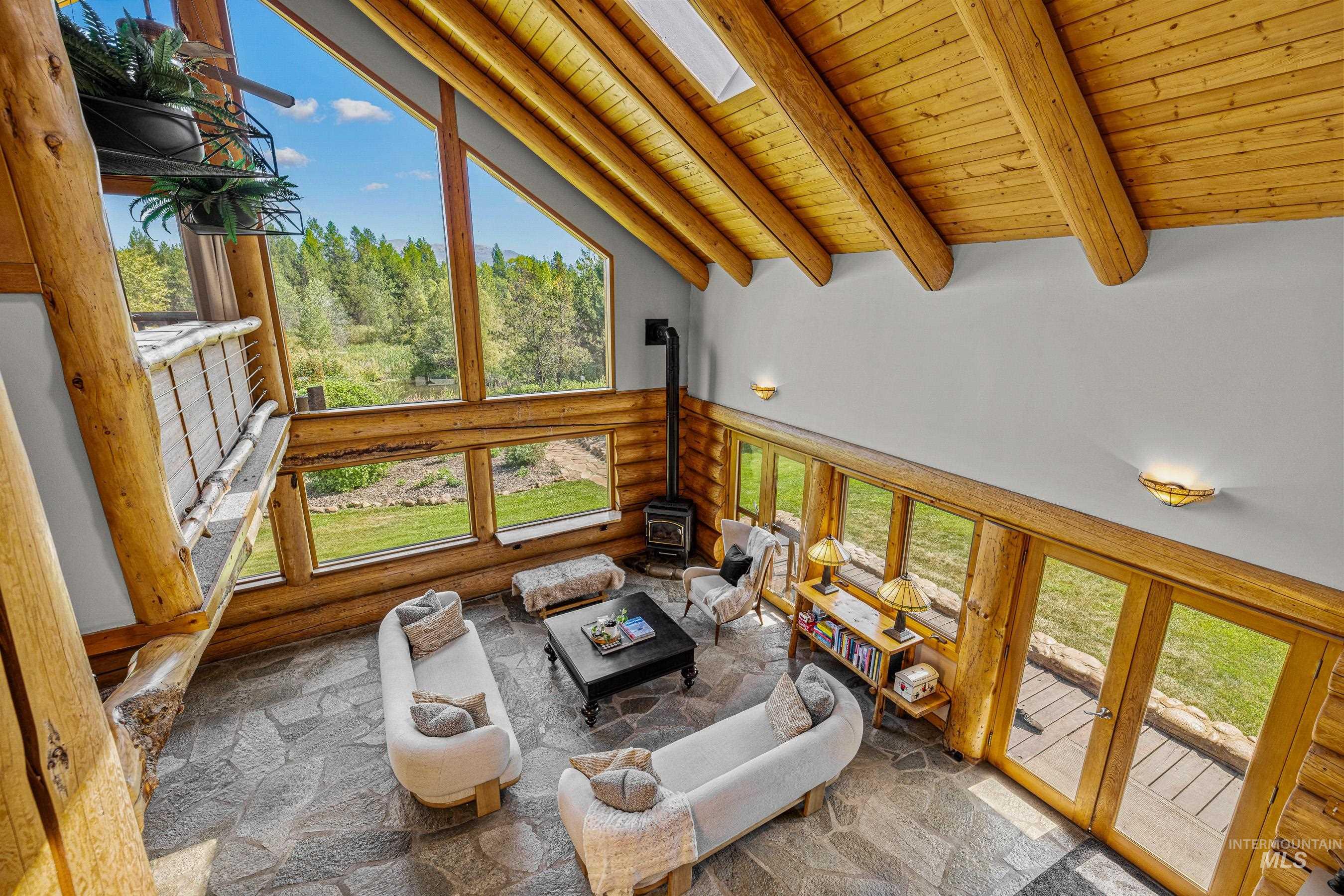 Living area with a wood stove, high vaulted ceiling, a wooden ceiling with exposed beams, healthy amount of natural light, and stone flooring