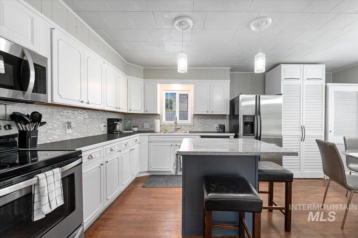 Kitchen with appliances with stainless steel finishes, pendant lighting, white cabinetry, a breakfast bar area, and ornamental molding