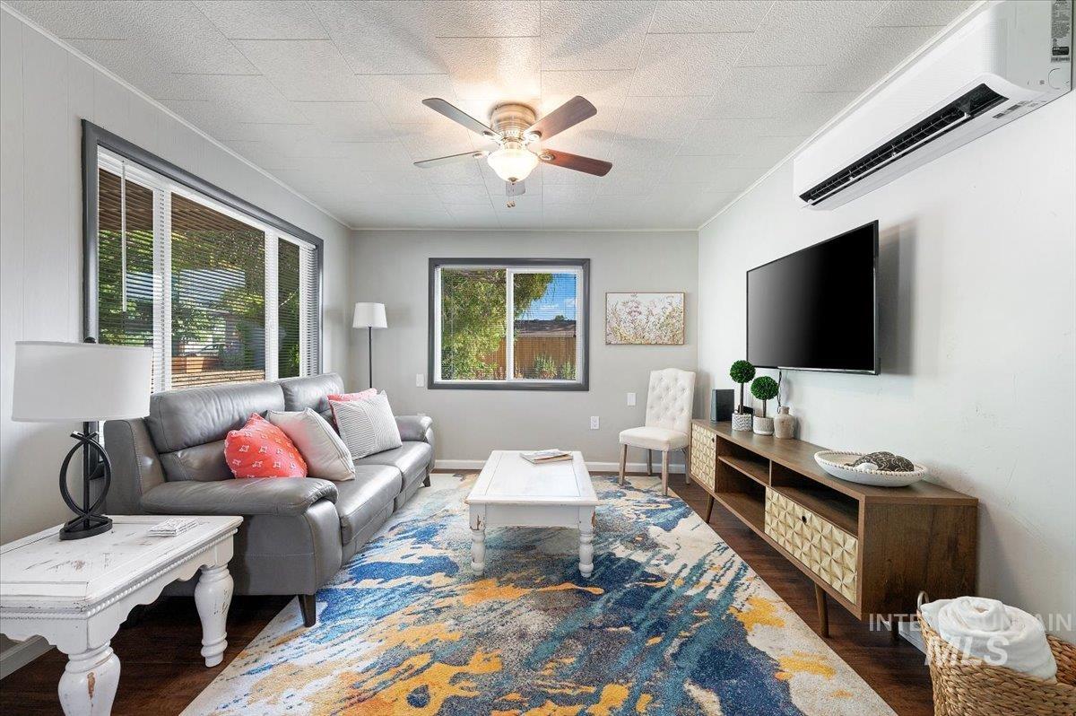 Living area featuring a wall mounted air conditioner, wood finished floors, ornamental molding, and ceiling fan