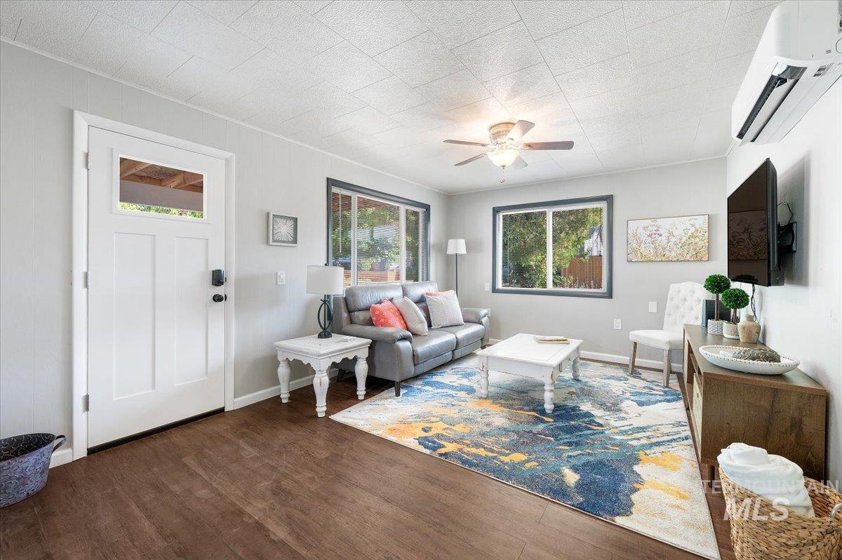 Living room with a wall mounted air conditioner, wood finished floors, a ceiling fan, and ornamental molding