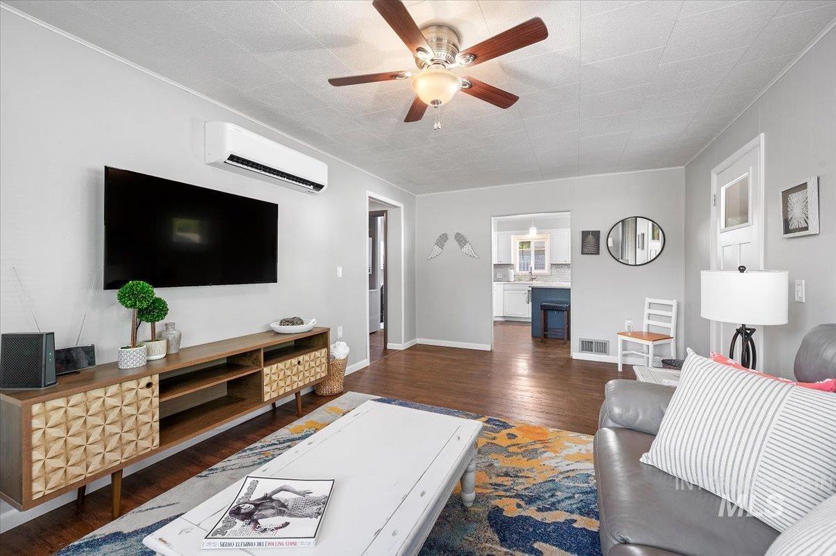 Living room with dark wood finished floors, a wall unit AC, and a ceiling fan