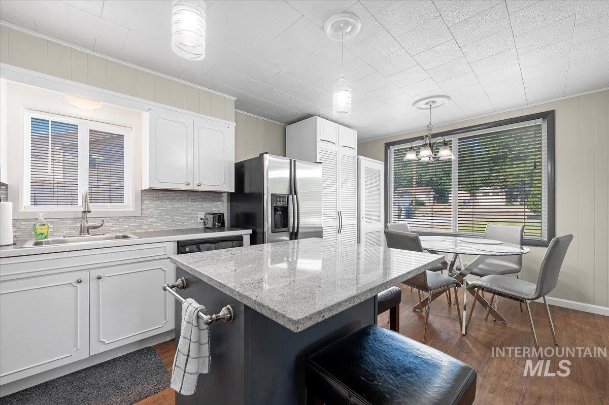 Kitchen featuring white cabinetry, light stone countertops, decorative light fixtures, a center island, and a kitchen bar
