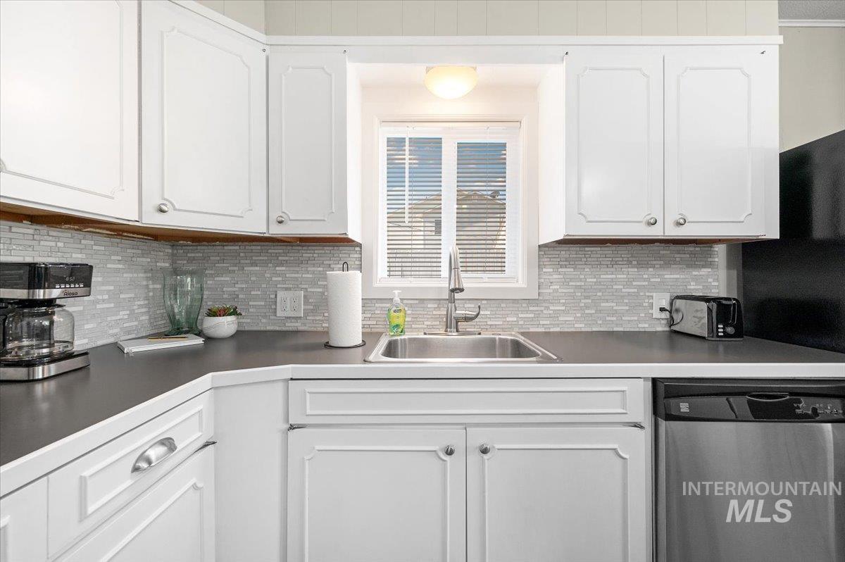 Kitchen with appliances with stainless steel finishes, backsplash, white cabinetry, and dark countertops