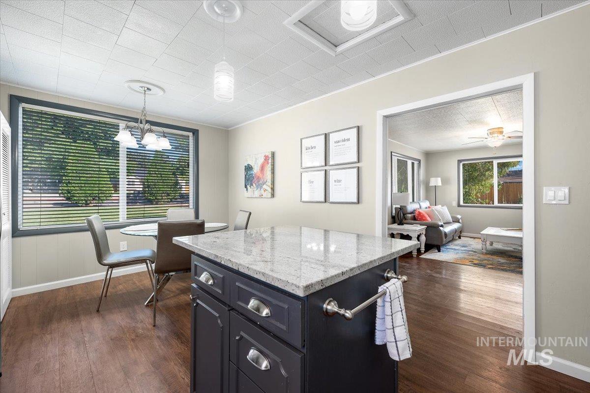 Kitchen with light stone counters, a kitchen island, decorative light fixtures, dark cabinets, and dark wood-type flooring
