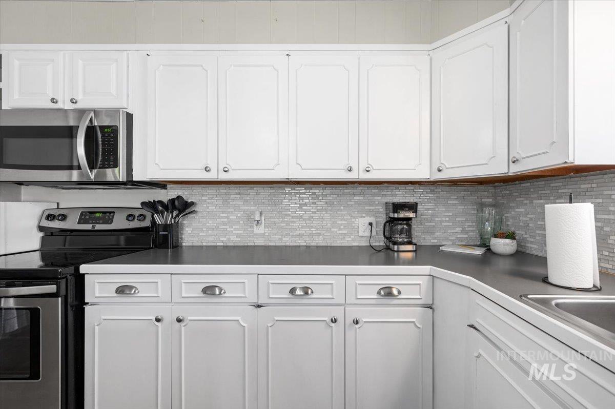 Kitchen featuring appliances with stainless steel finishes, white cabinetry, and backsplash