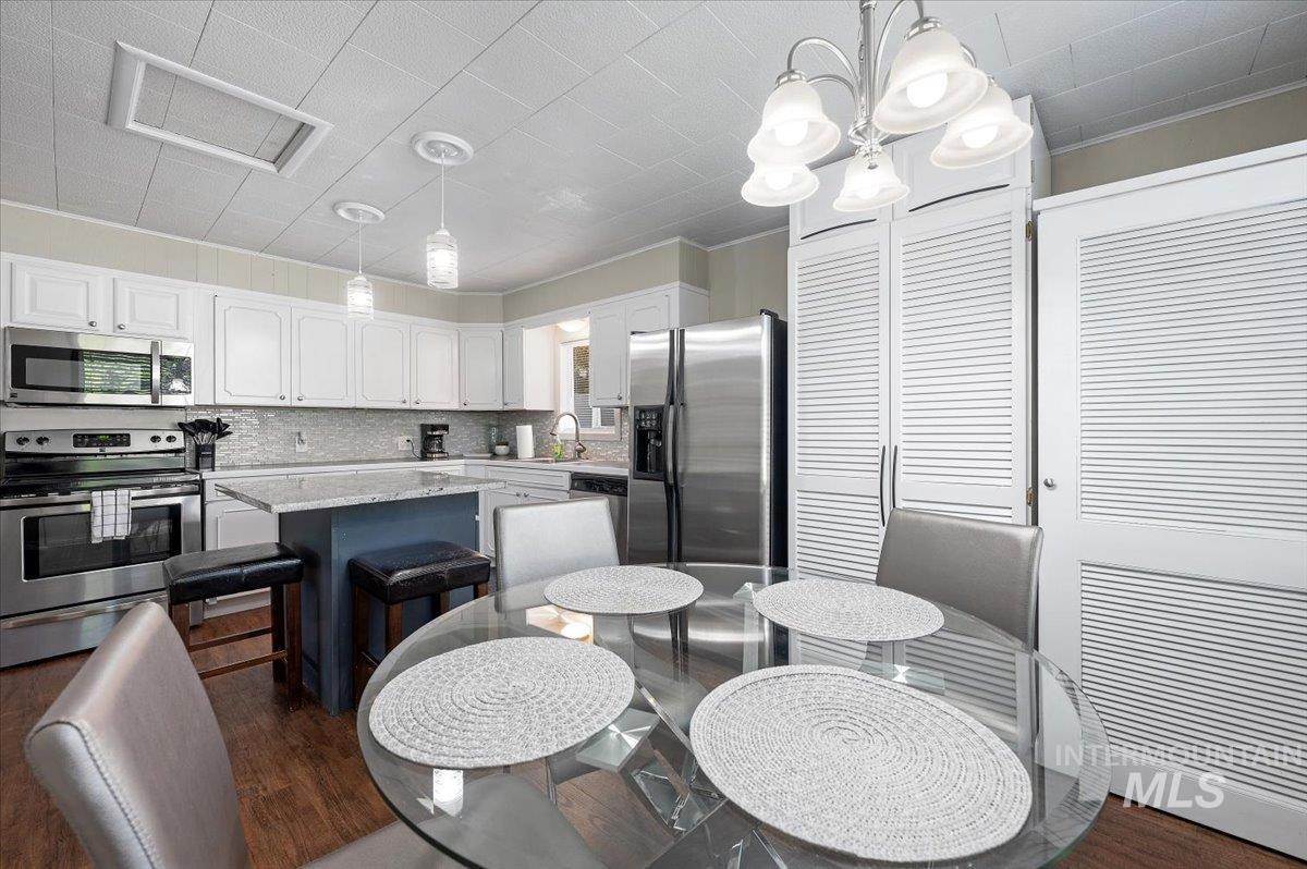 Kitchen with appliances with stainless steel finishes, hanging light fixtures, white cabinetry, dark wood finished floors, and decorative backsplash