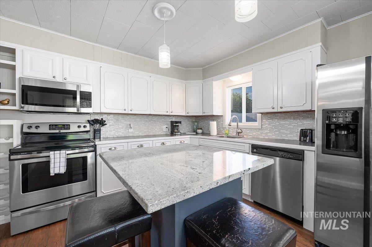 Kitchen with stainless steel appliances, hanging light fixtures, light stone countertops, a center island, and a kitchen bar