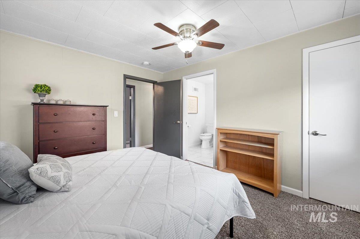 Bedroom with dark carpet, a ceiling fan, and ensuite bath