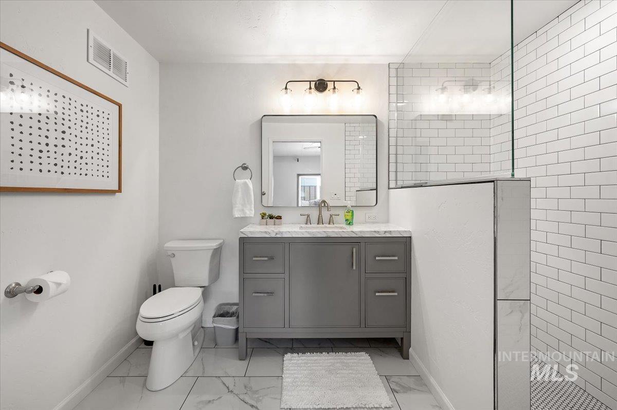 Bathroom with walk in shower, vanity, and light marble finish flooring