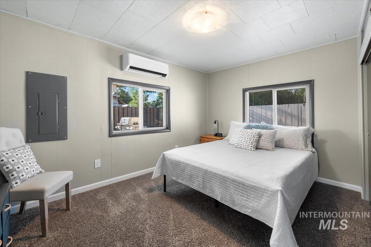 Carpeted bedroom with electric panel, a wall unit AC, and wood walls