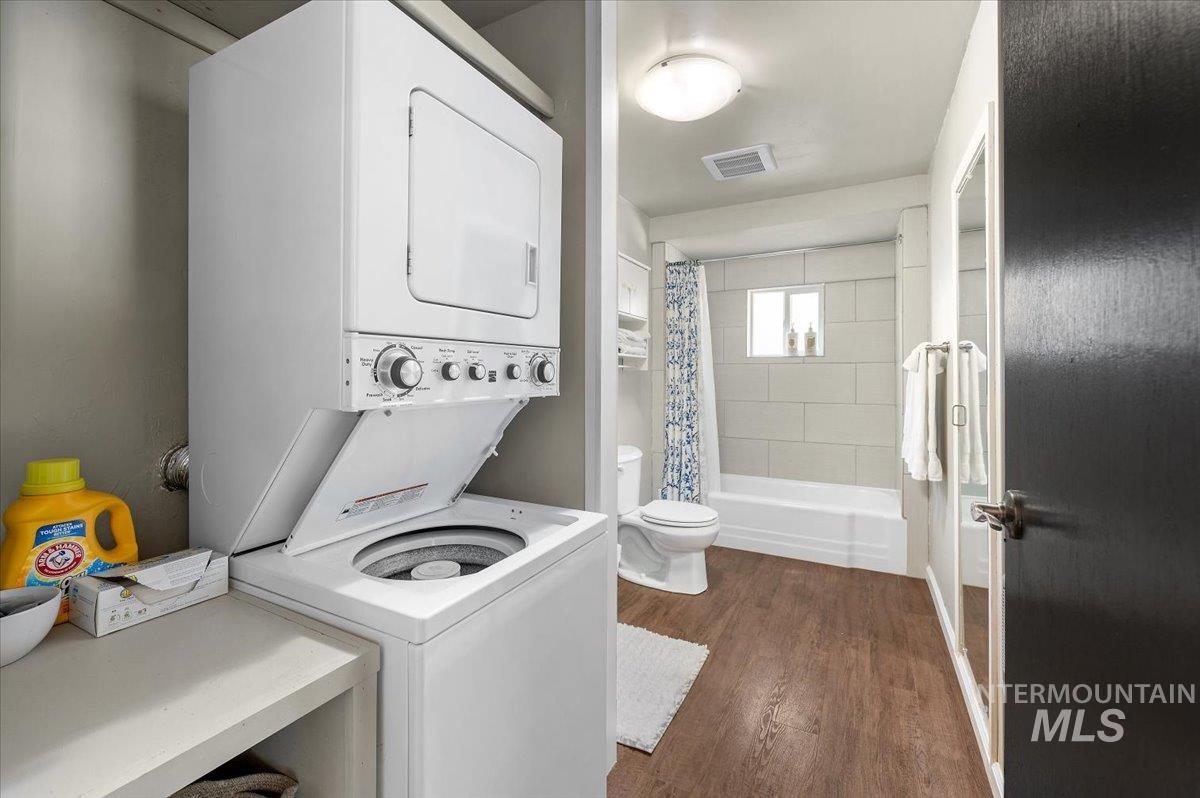 Washroom with dark wood-style floors and stacked washer / dryer