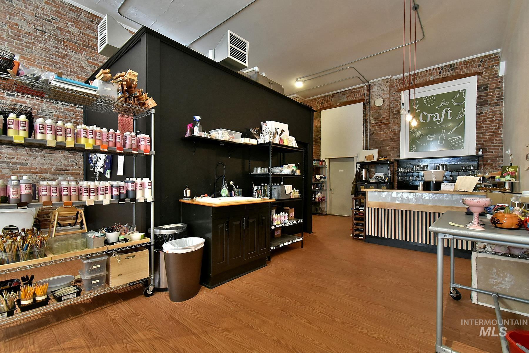 Interior space featuring brick wall, light wood finished floors, pendant lighting, a high ceiling, and dark cabinets