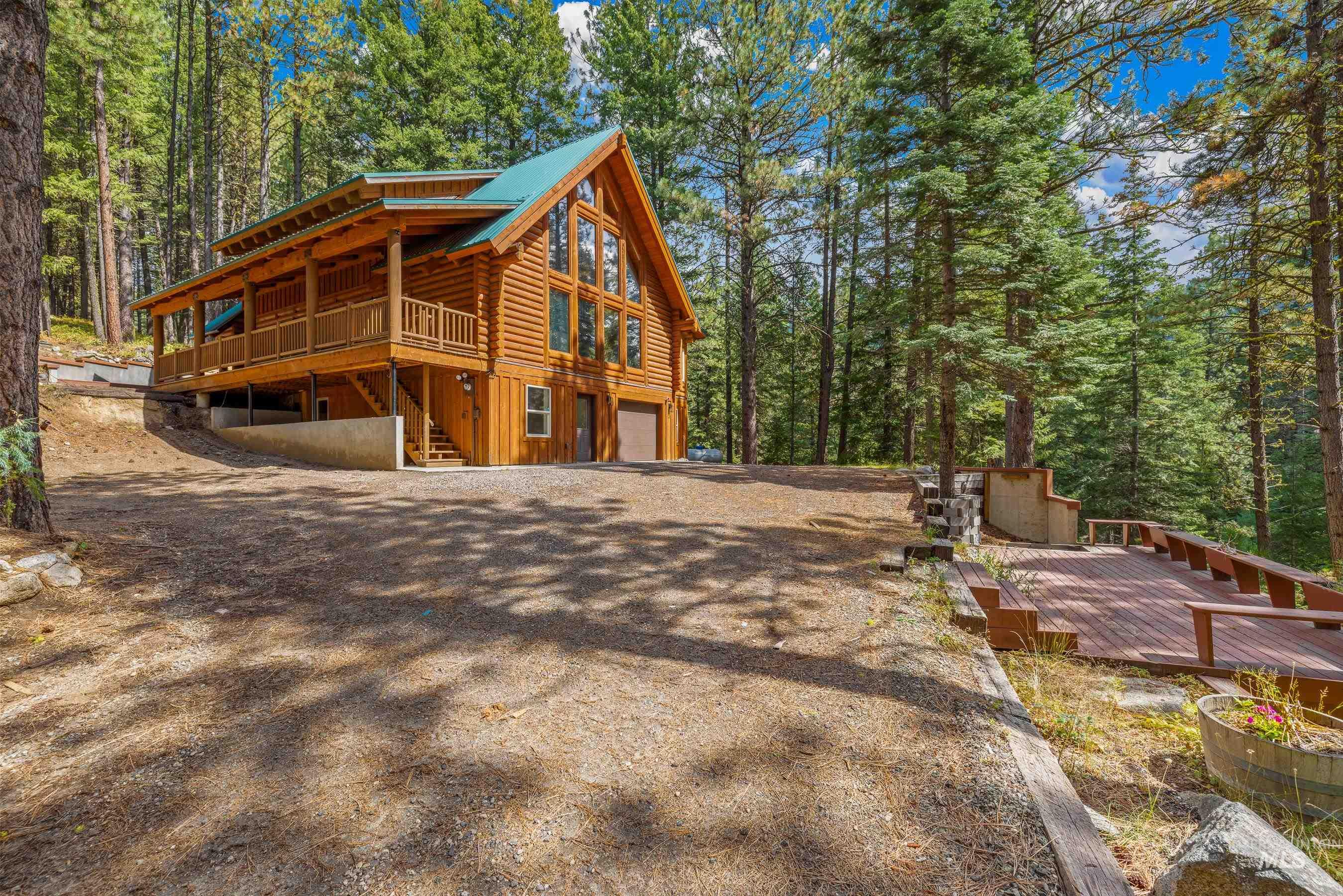 View of property exterior featuring a wooden deck, log siding, a garage, a view of trees, and stairway