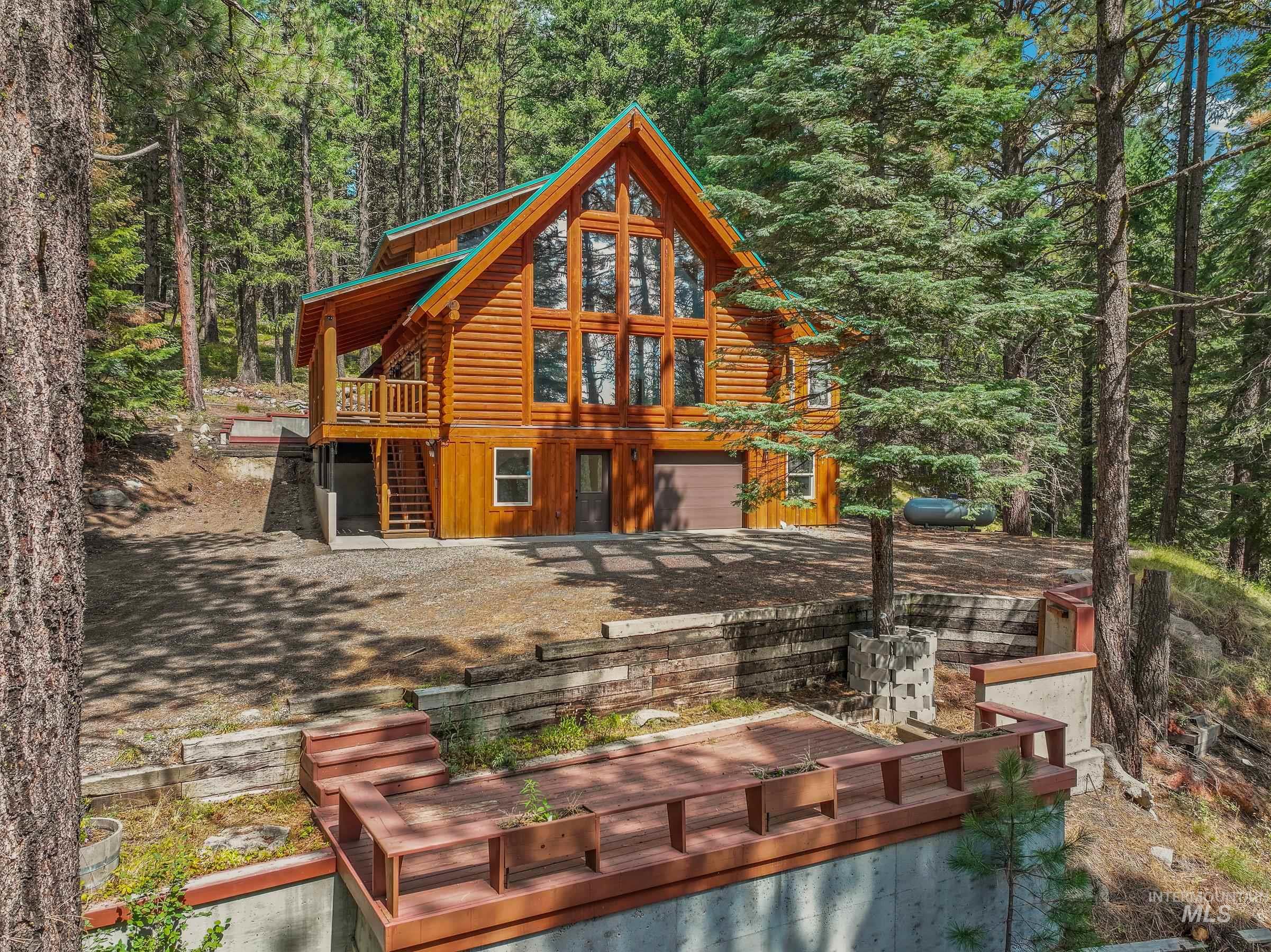 Back of house featuring a deck, a wooded view, log exterior, and driveway