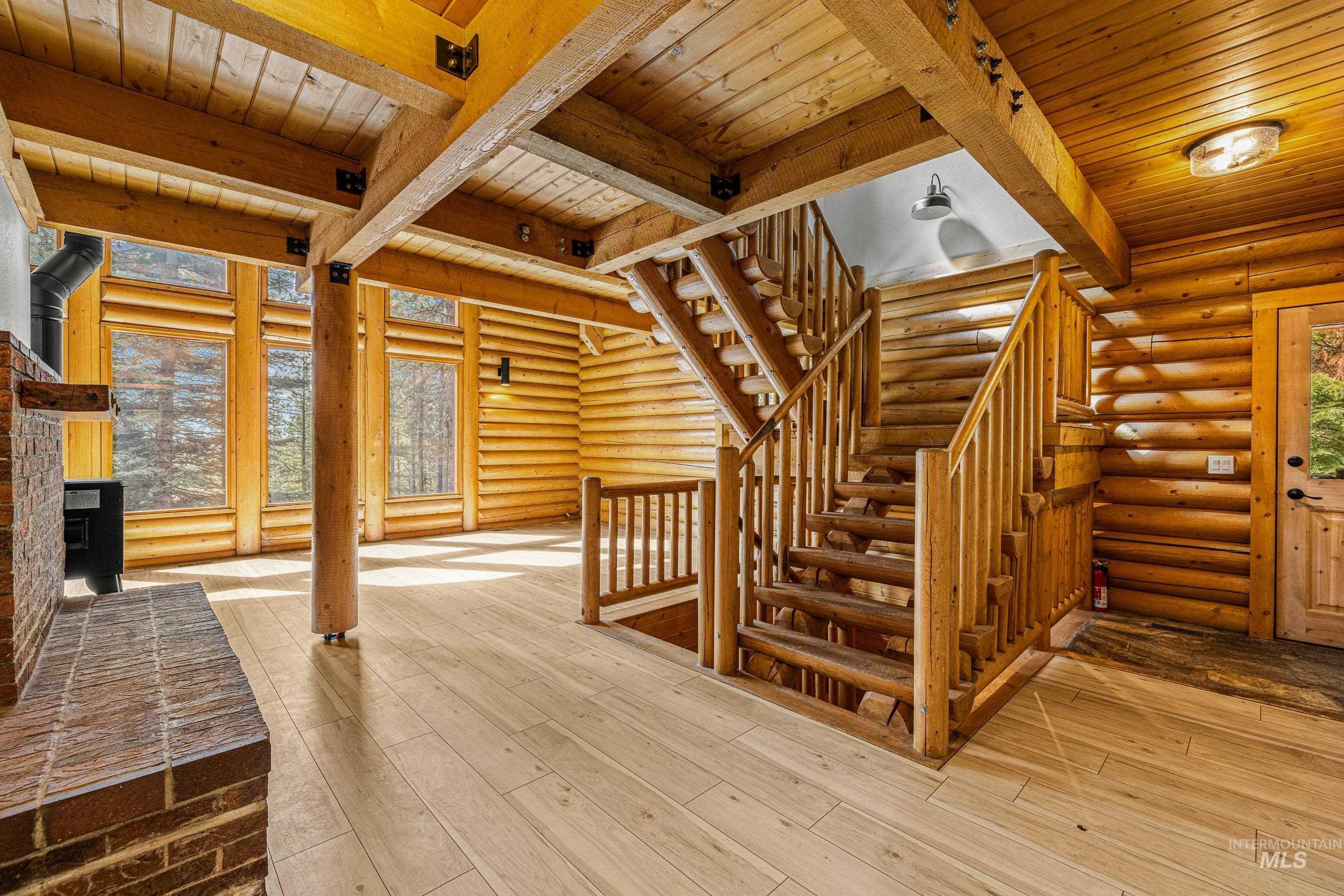 Stairs with a wood stove, a wood ceiling with exposed beams, hardwood / wood-style floors, and log walls