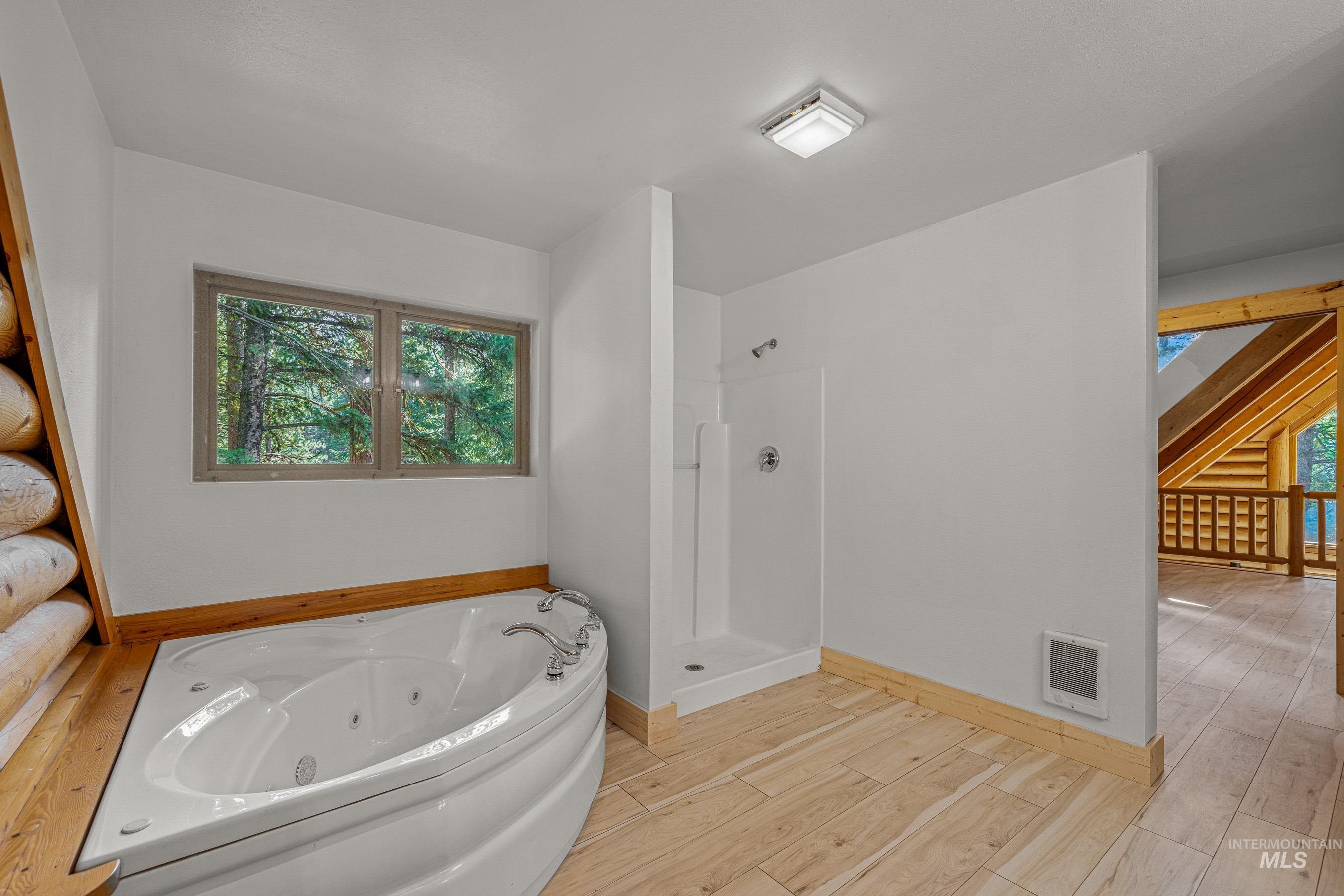 Full bathroom with light wood-style floors, a jetted tub, a shower stall, and heating unit