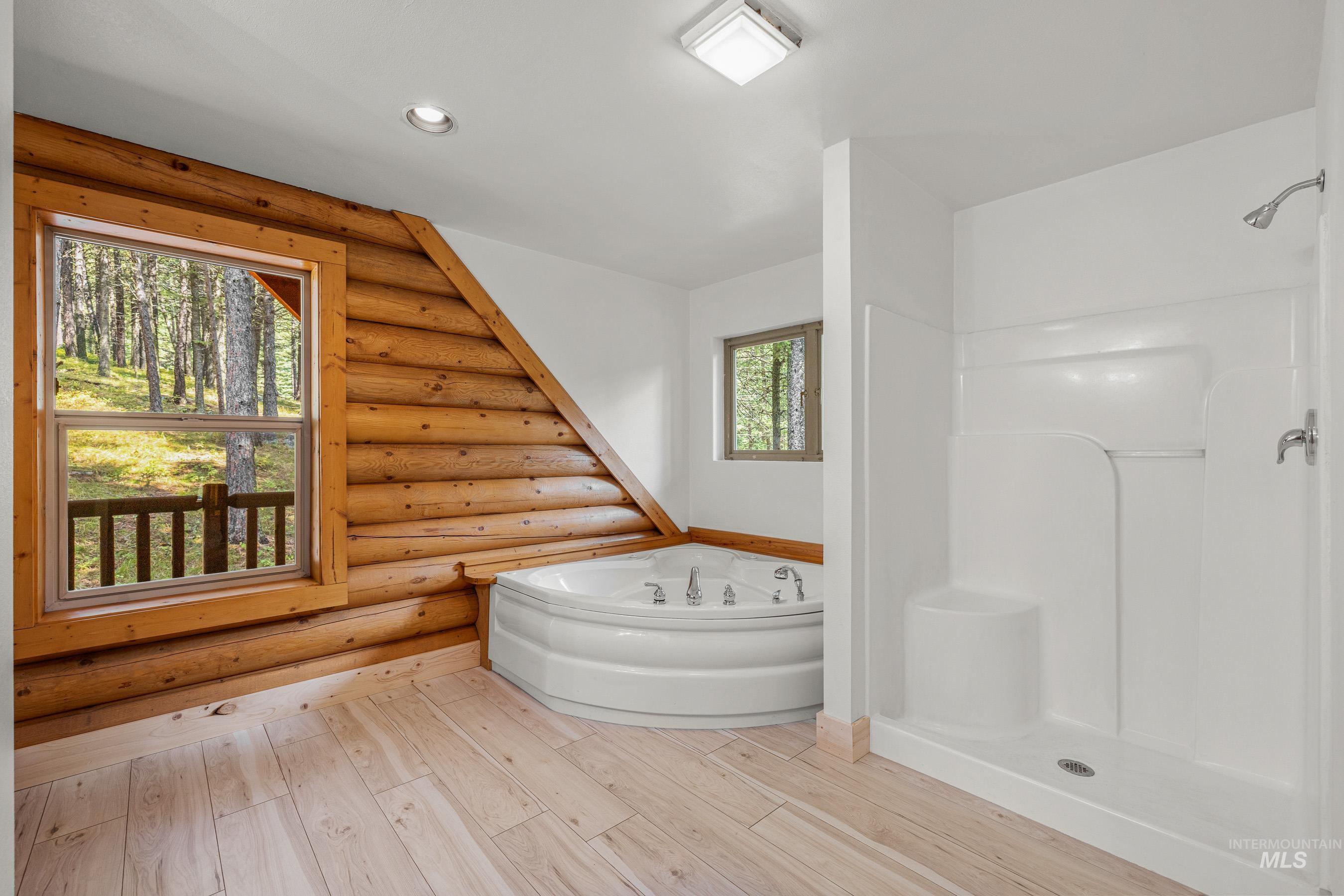 Full bath featuring a stall shower, a bath, wood finished floors, recessed lighting, and log walls