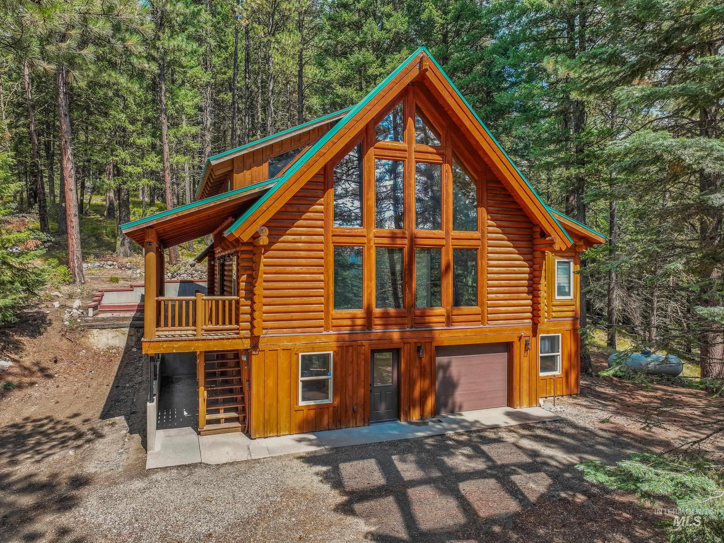 Cabin featuring log siding, a garage, stairs, driveway, and a view of trees