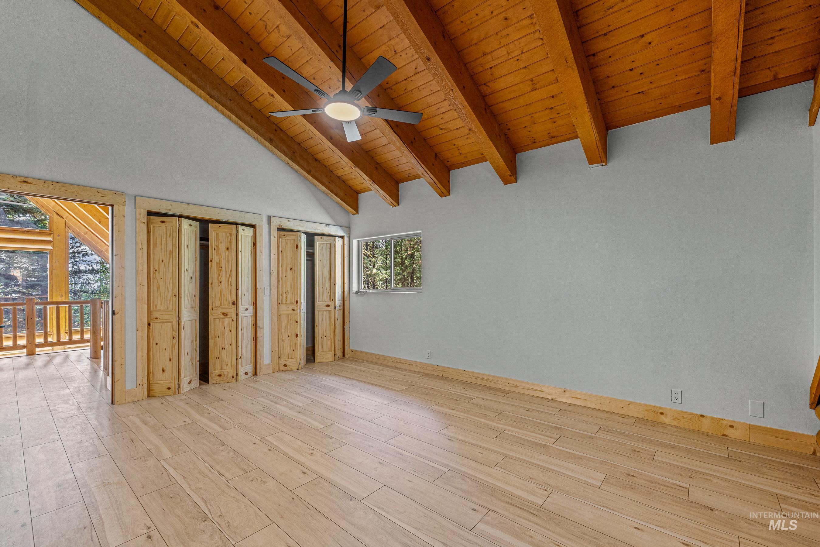 Unfurnished bedroom with a wood ceiling with exposed beams, high vaulted ceiling, two closets, light wood finished floors, and ceiling fan