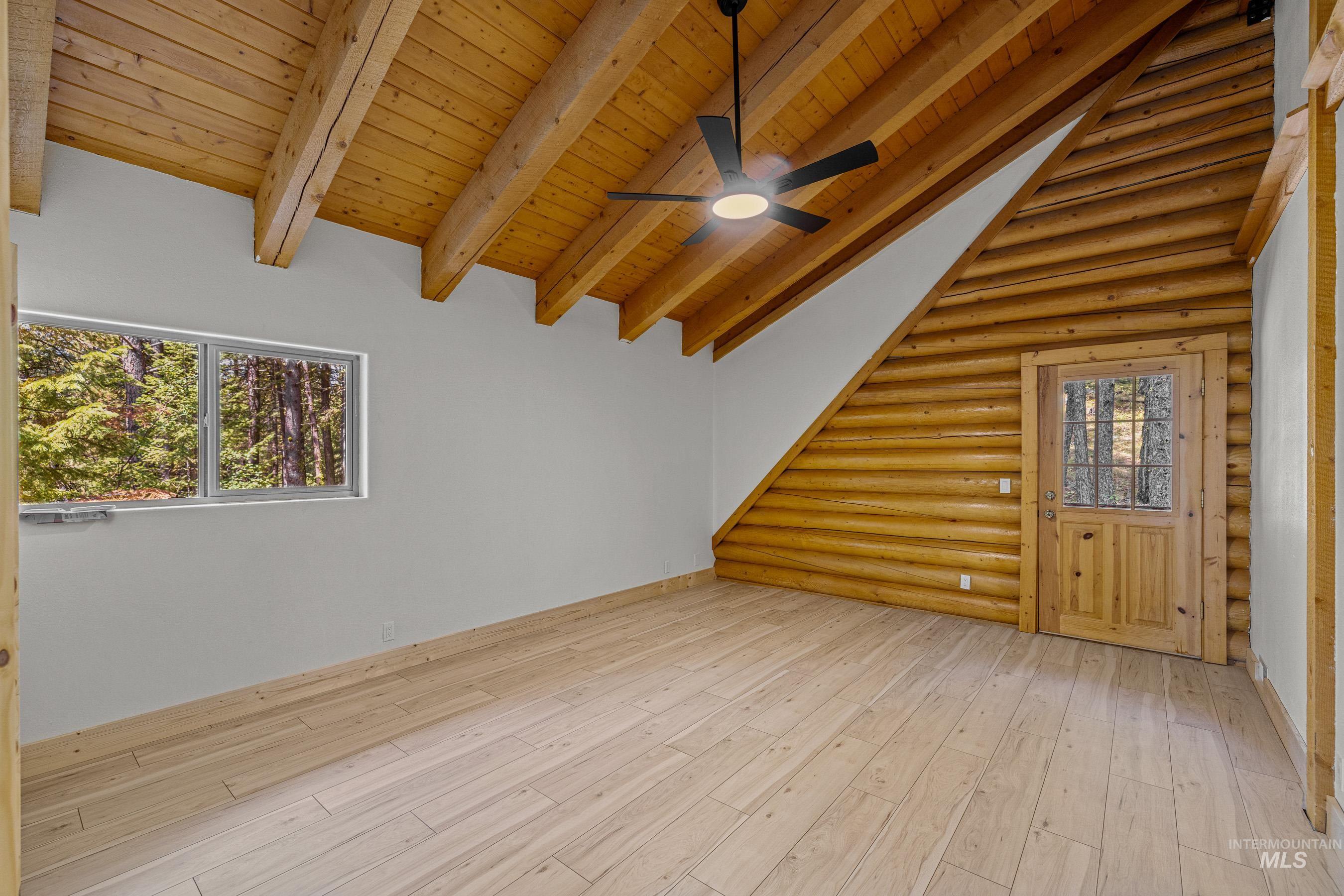 Unfurnished living room featuring light wood-style flooring, wood ceiling, a ceiling fan, log walls, and stairs