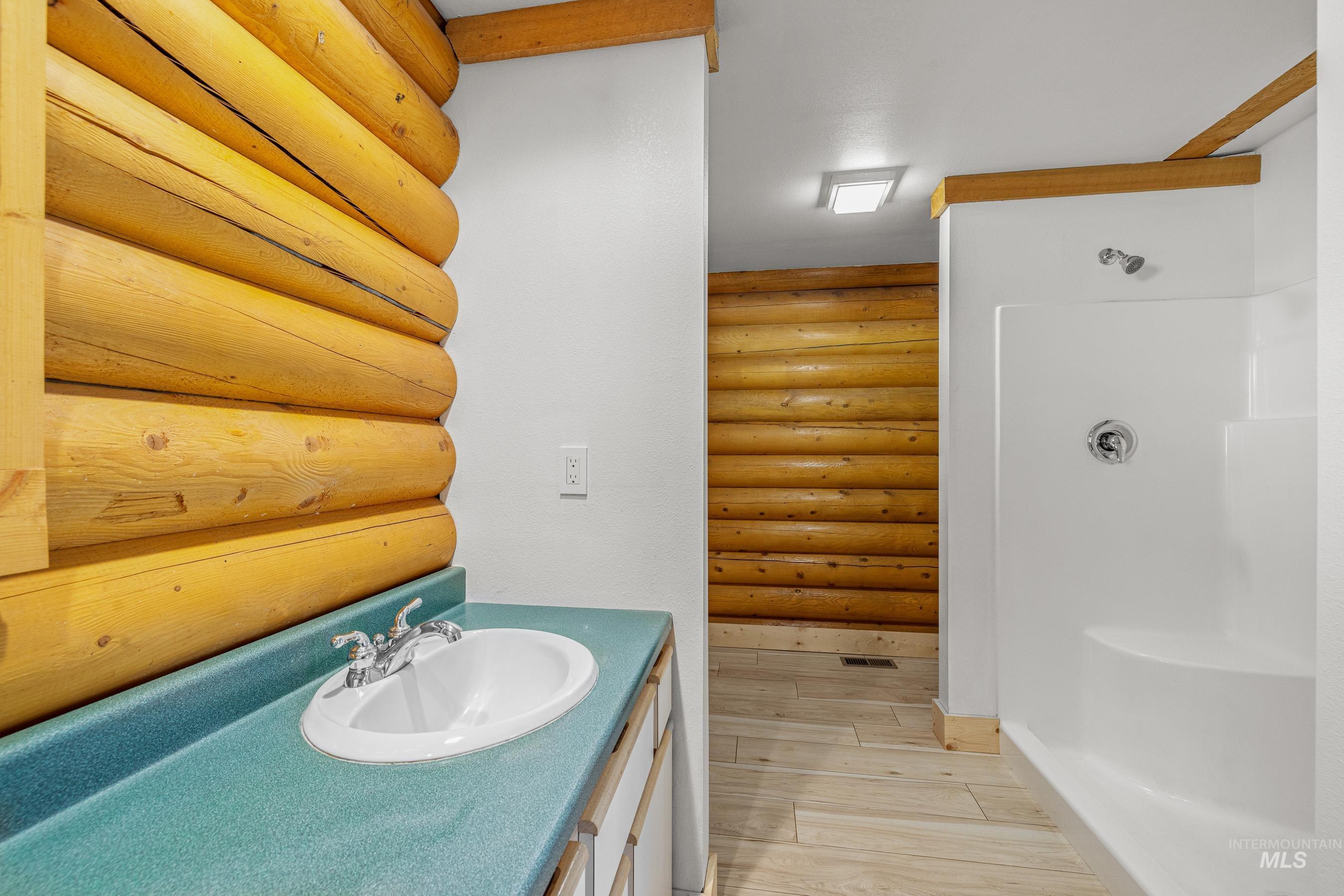 Full bathroom with wood tiled floors, vanity, a stall shower, and log walls