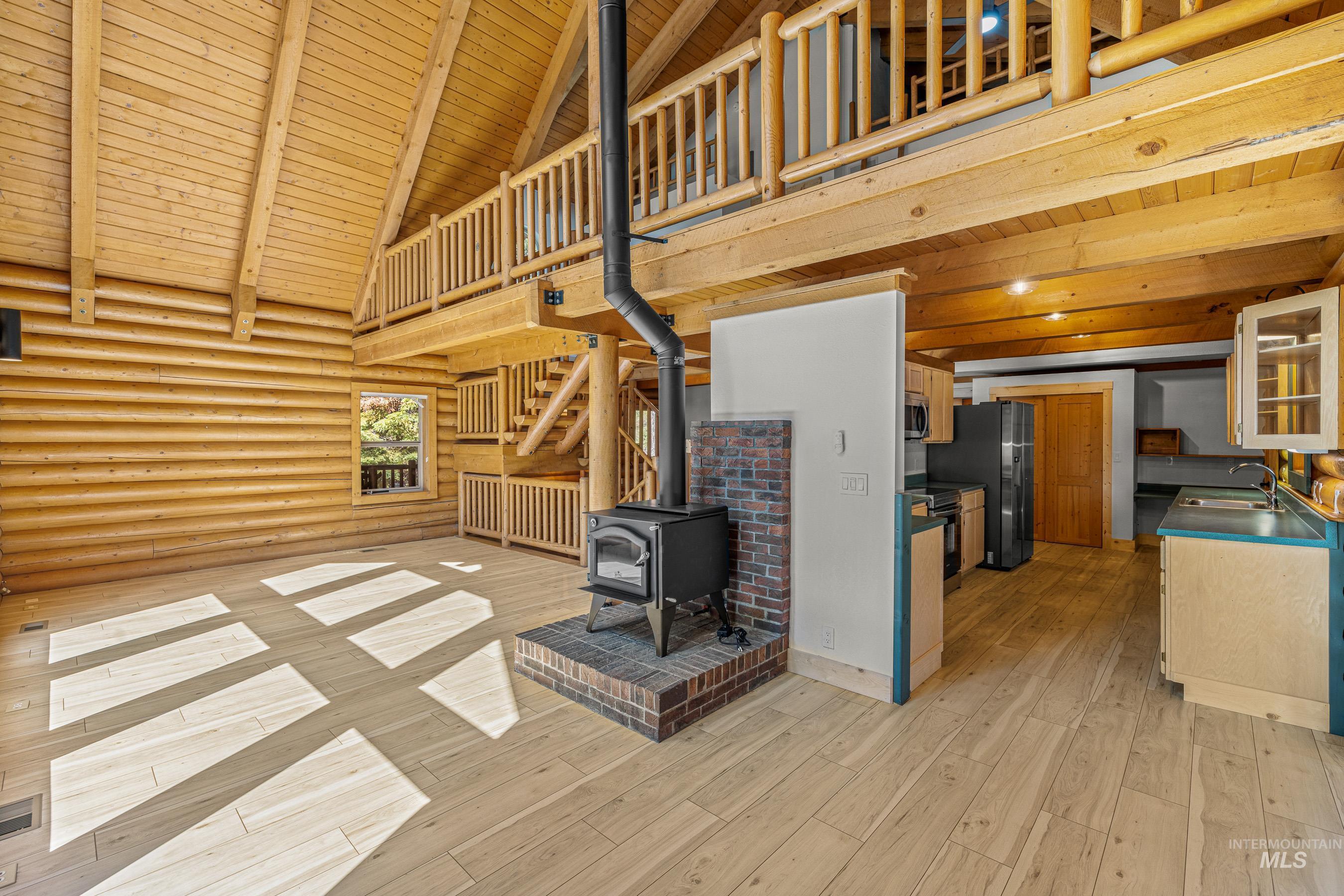 Unfurnished living room with a wooden ceiling with exposed beams, rustic walls, high vaulted ceiling, a wood stove, and light wood-type flooring