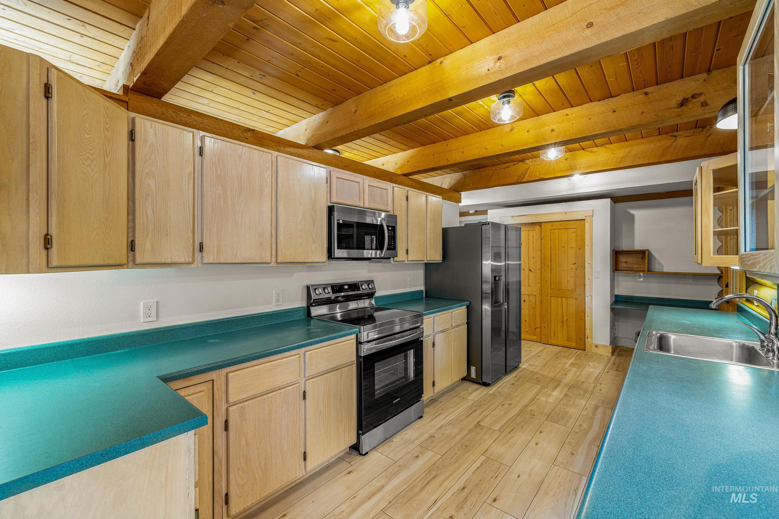 Kitchen featuring stainless steel appliances, light brown cabinetry, light wood-style flooring, glass insert cabinets, and a wooden ceiling with exposed beams