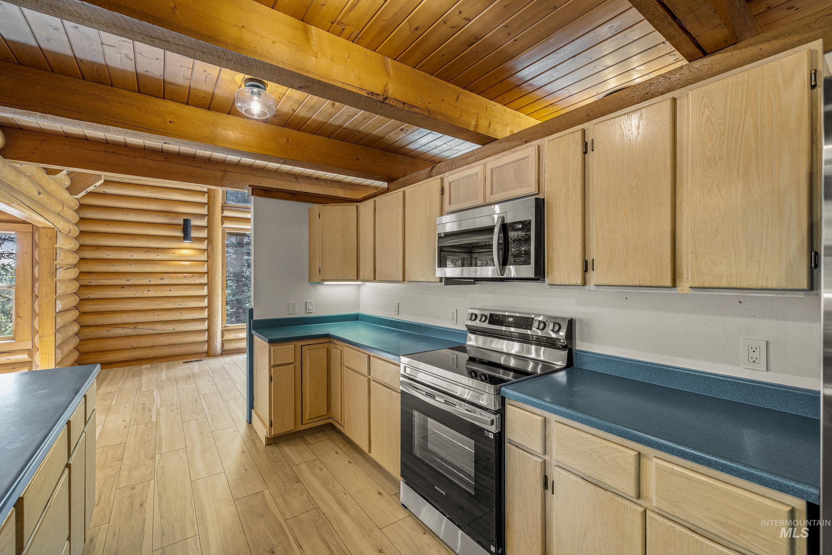 Kitchen featuring log walls, appliances with stainless steel finishes, light brown cabinets, dark countertops, and light wood-type flooring