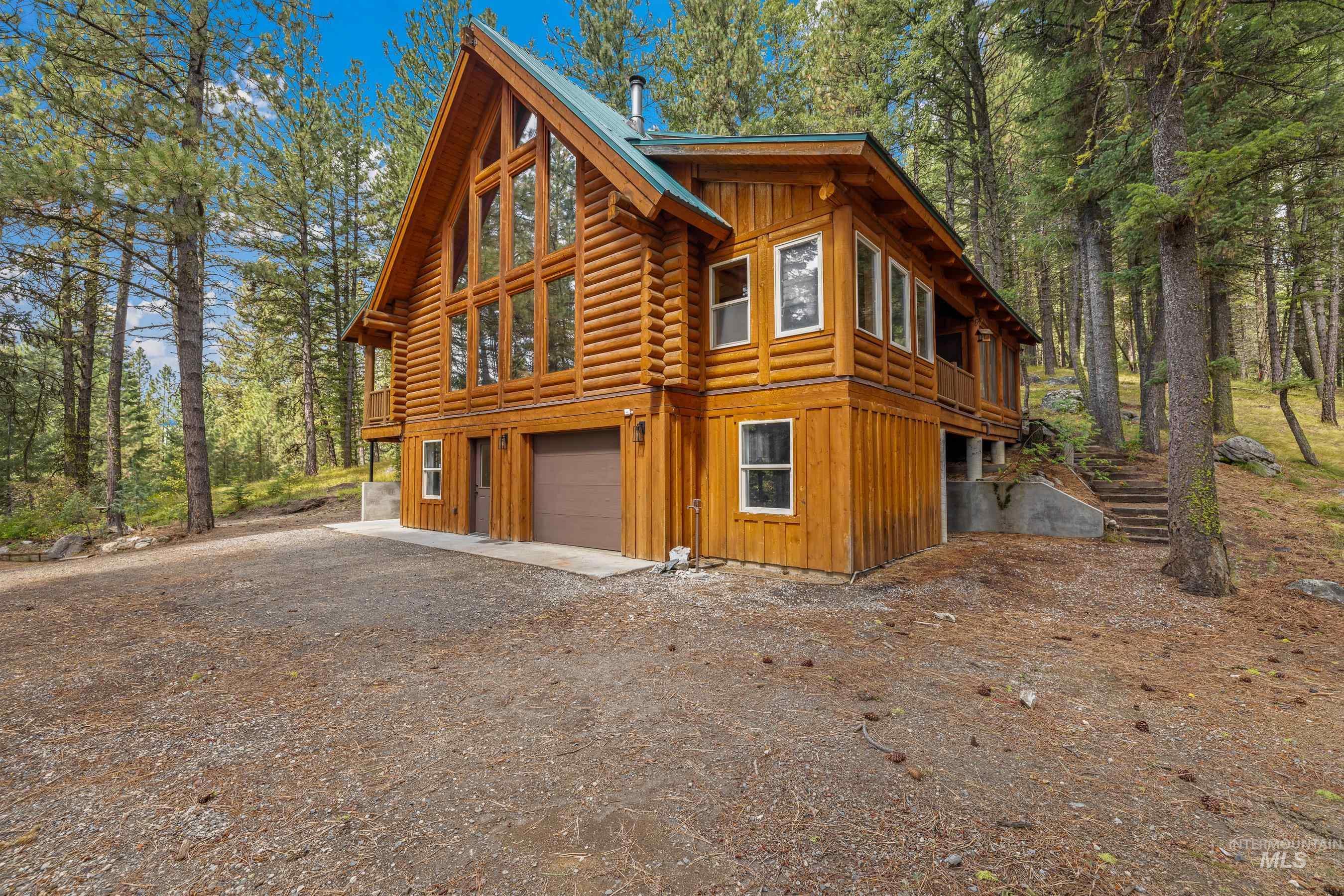 View of home's exterior with board and batten siding, log exterior, an attached garage, driveway, and a forest view