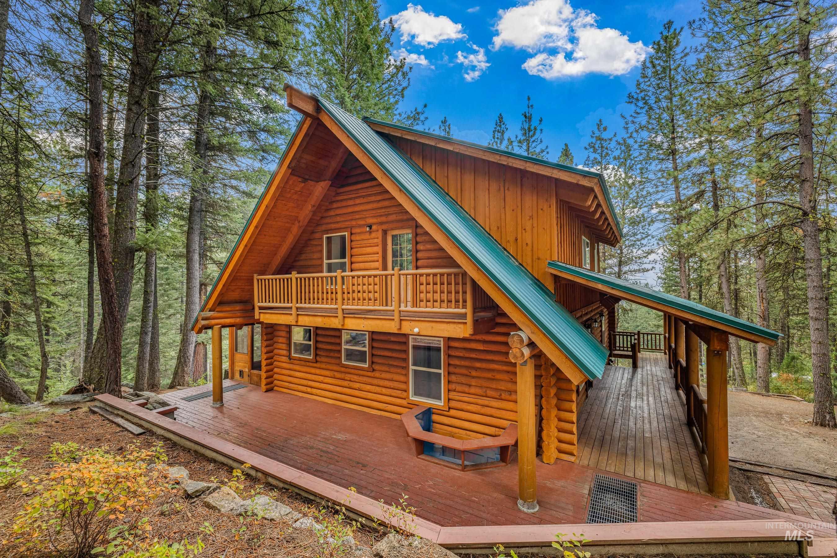 Rear view of house with log exterior, a wooden deck, a metal roof, and a forest view