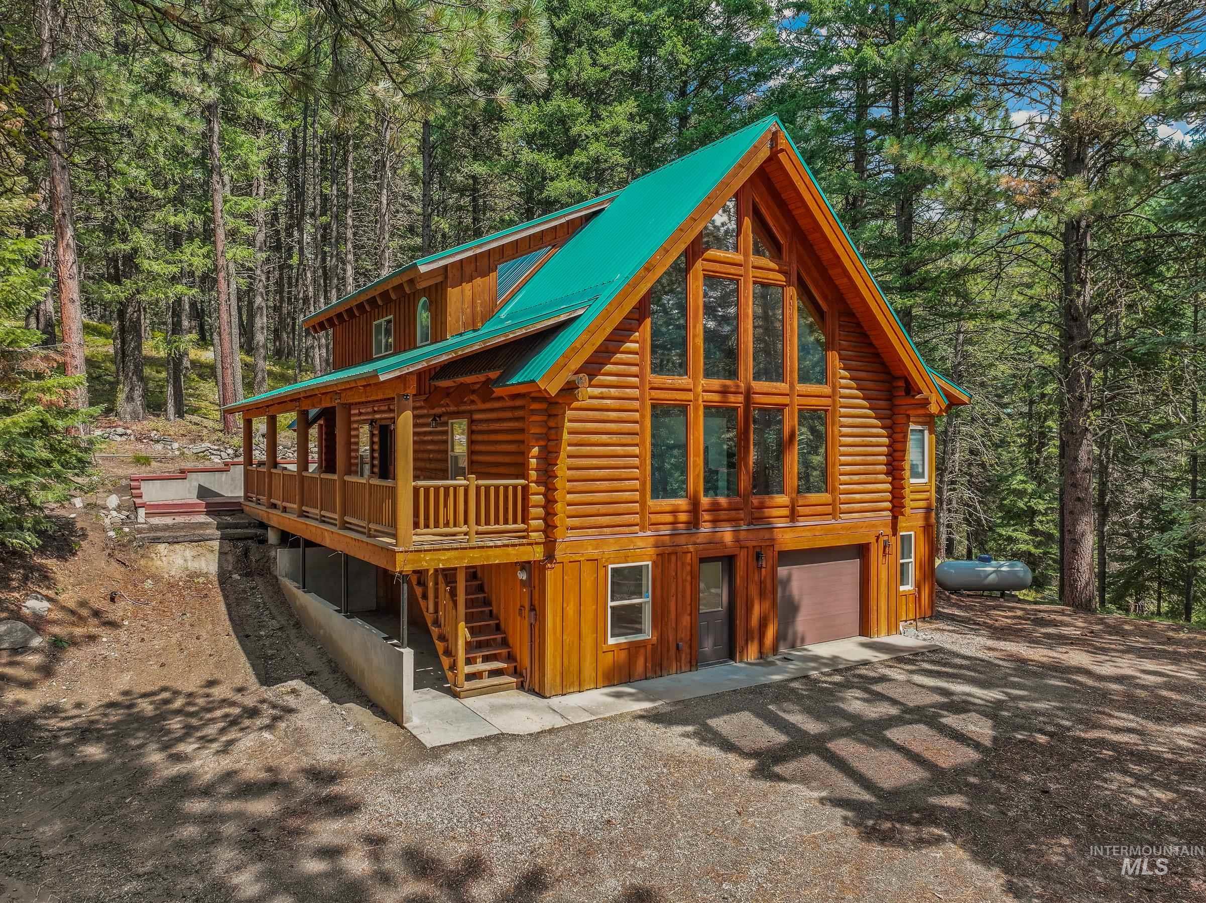 View of front of property featuring log exterior, stairway, an attached garage, a metal roof, and a wooded view