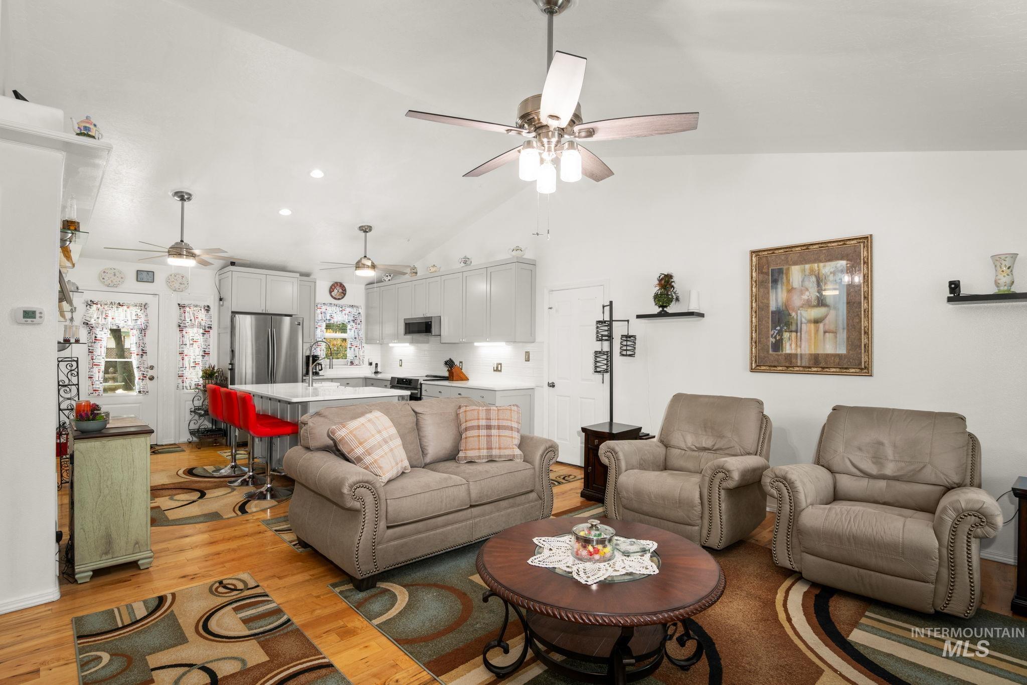 Living room with light wood finished floors, ceiling fan, high vaulted ceiling, and recessed lighting
