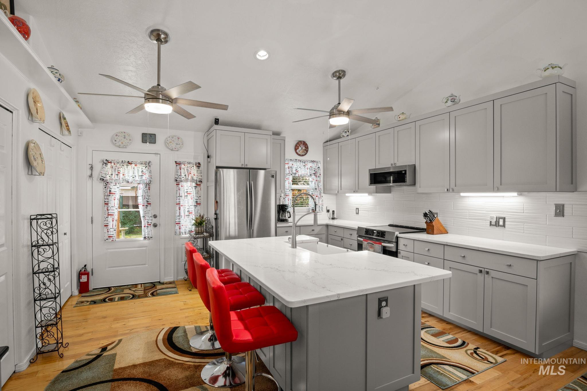 Kitchen with gray cabinetry, light wood-type flooring, light stone counters, stainless steel appliances, and a kitchen breakfast bar