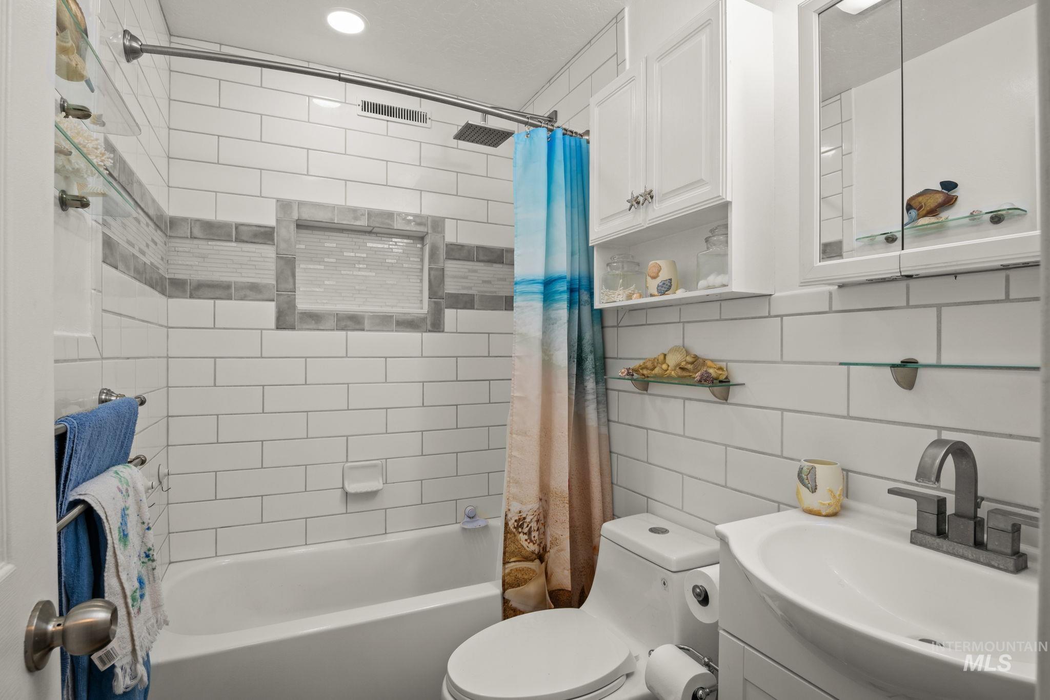 Full bathroom featuring shower / bathtub combination with curtain, vanity, tasteful backsplash, and tile walls