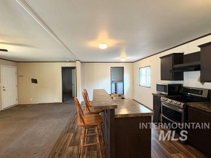 Kitchen with appliances with stainless steel finishes, a breakfast bar, washing machine and clothes dryer, a kitchen island with sink, and dark countertops