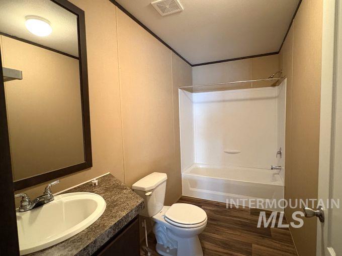 Full bath featuring dark wood-type flooring, vanity, bathing tub / shower combination, and ornamental molding