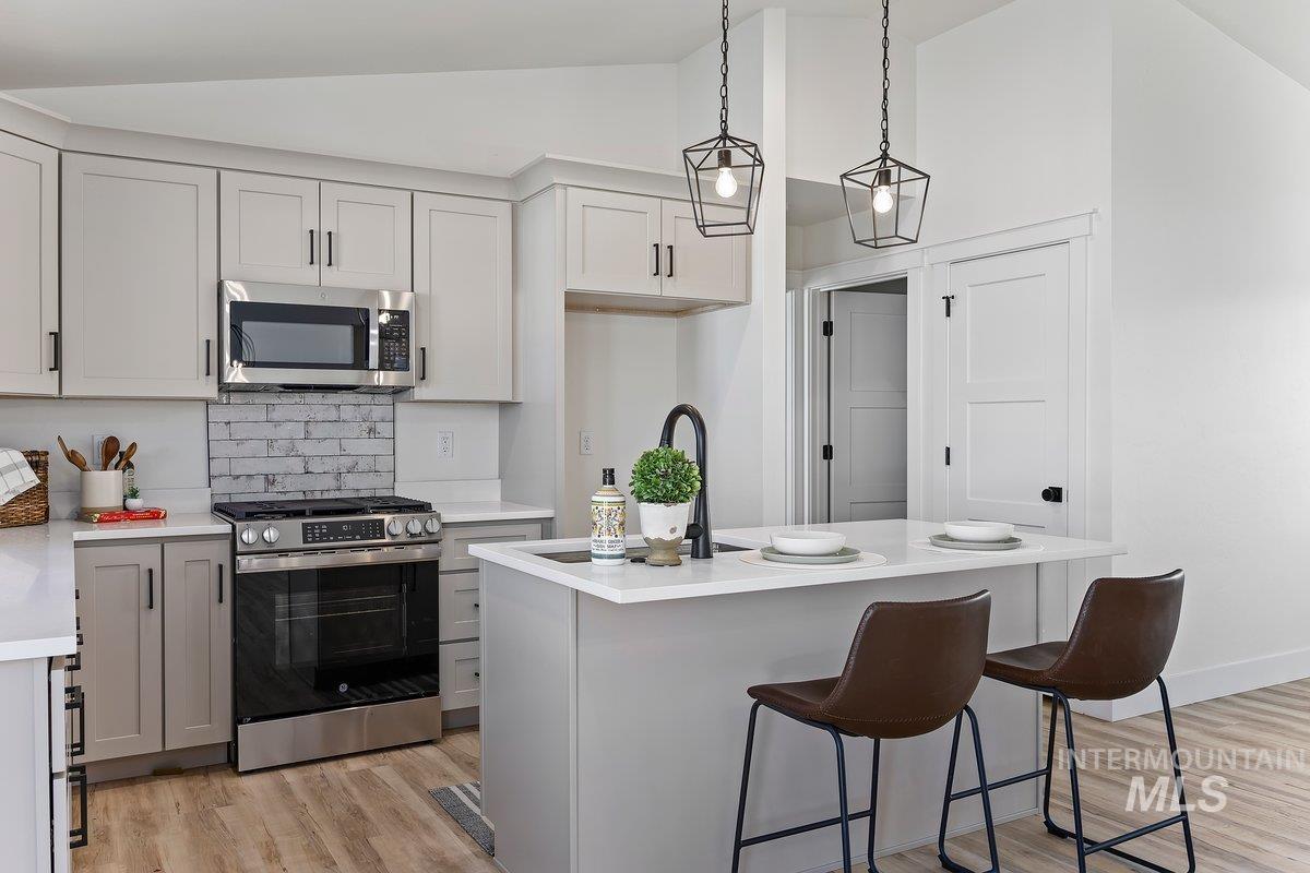 Kitchen featuring appliances with stainless steel finishes, a kitchen bar, light wood-style floors, decorative light fixtures, and a kitchen island with sink